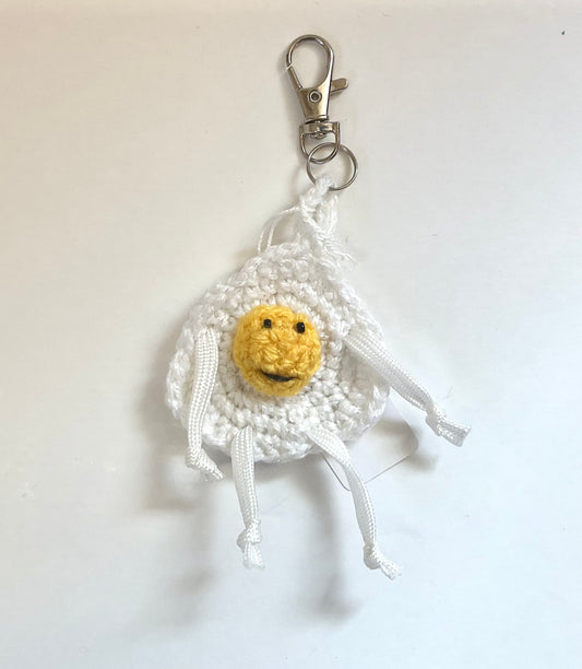 Crocheted egg keychain with a smiling yolk face, and arms and legs, on a white background