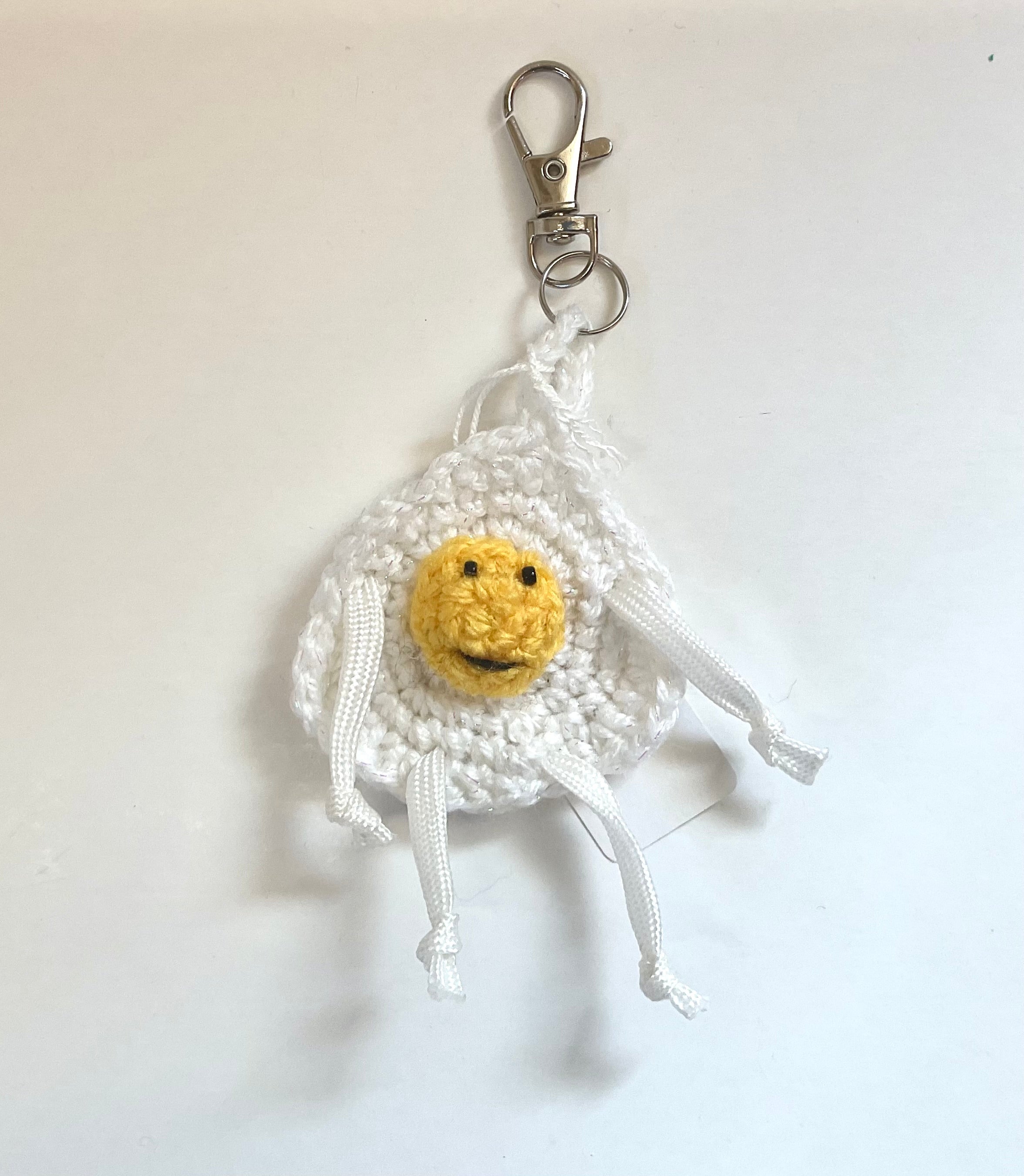Crocheted egg keychain with a smiling yolk face, and arms and legs, on a white background