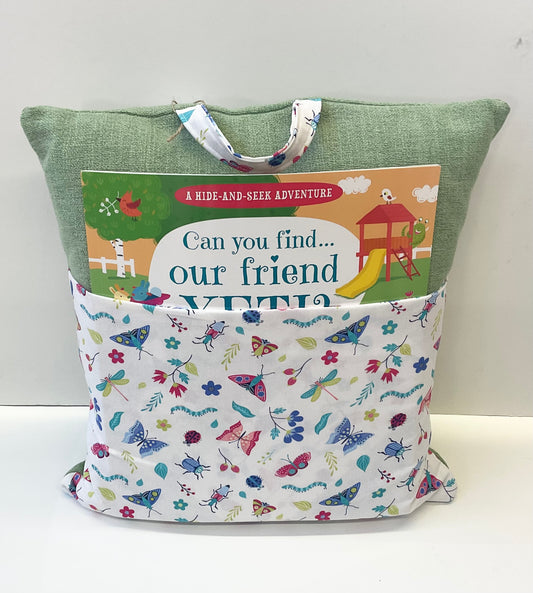 A green pillow with a butterfly and flower patterned pocket containing a childrens book