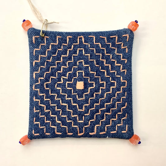 Decoratively stitched denim coaster with a geometric pattern and beads on each corner