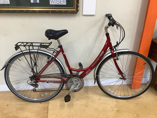 Red bicycle with a black saddle on a wooden floor against a white wall.