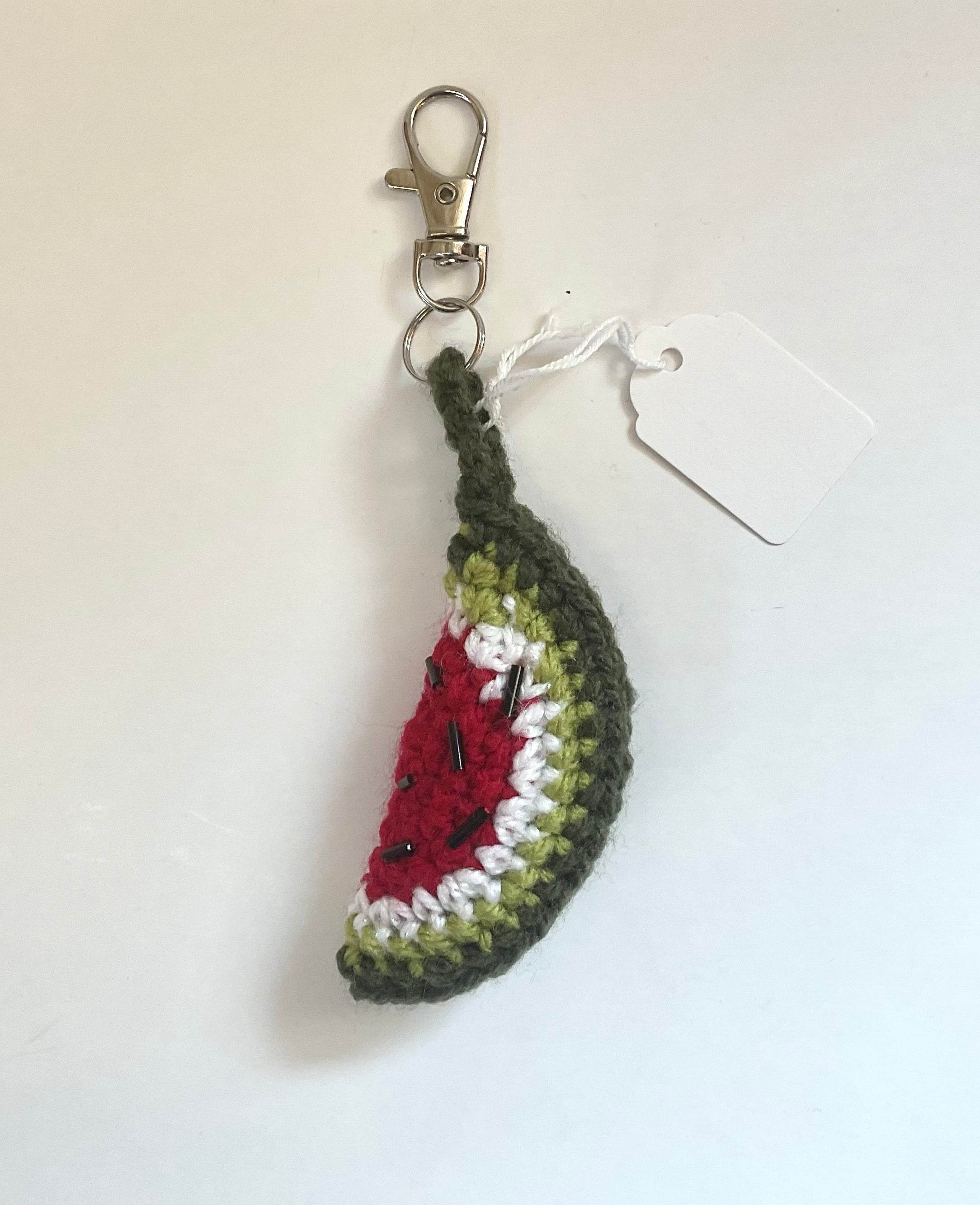 Crocheted watermelon slice keychain with black seeds made from beads on a white background