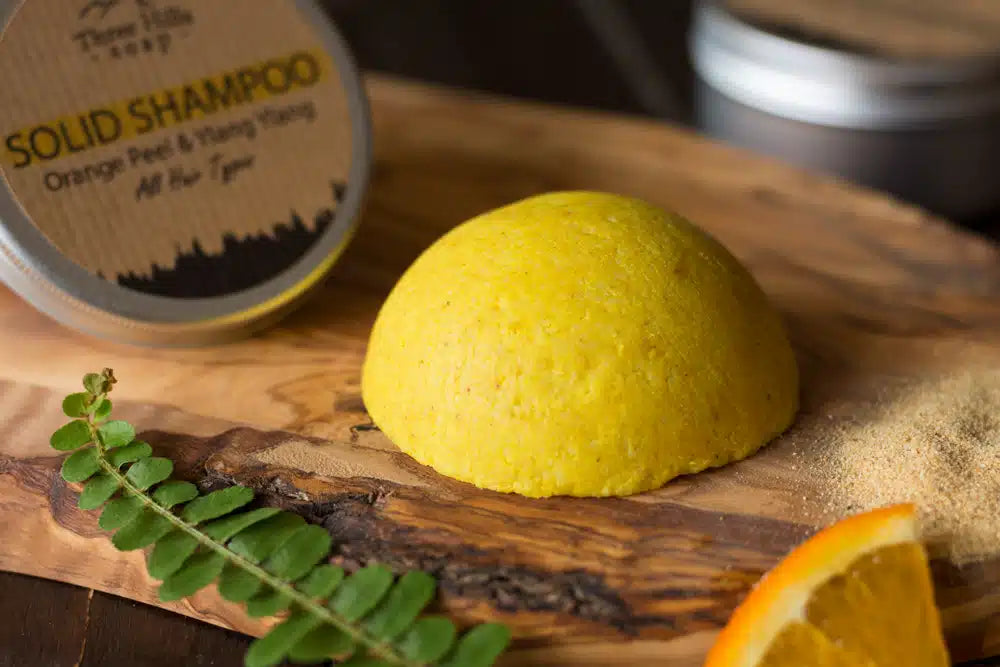 Yellow solid shampoo bar on a wooden board with a metal container labeled 'Solid Shampoo' in the background.