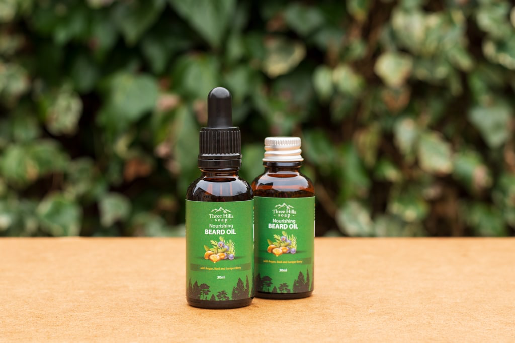 Two glass bottles of beard oil on a wooden surface with a green leafy background