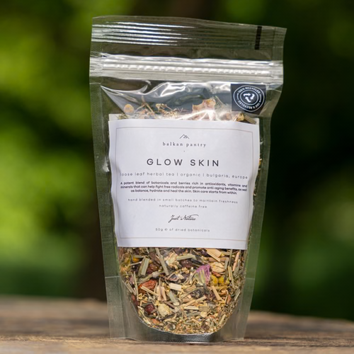 Herbal tea package labeled 'Glow Skin' by hulka pantry on a wooden surface with a blurred green background.