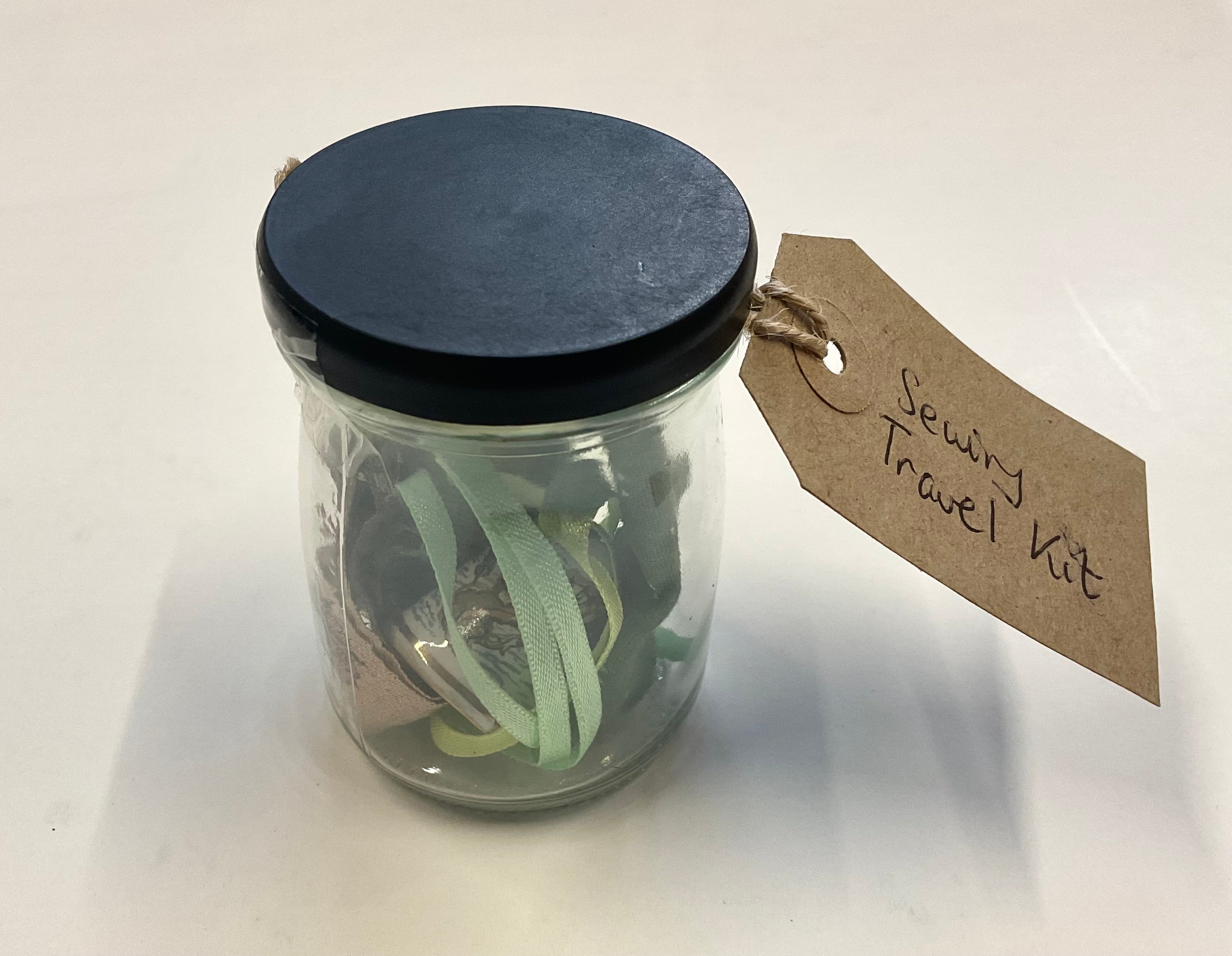 Glass jar with black lid containing sewing supplies and a 'Sewing Travel Kit' tag on a white background