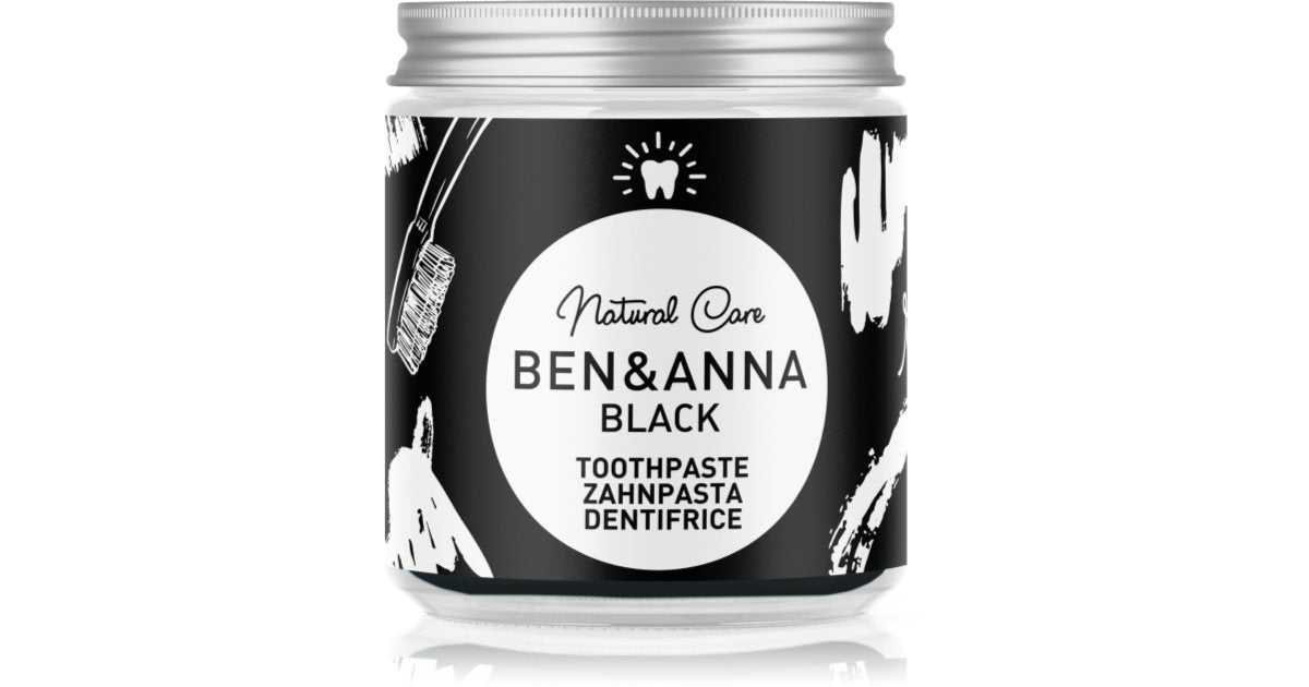 A jar of Ben & Anna Black Natural Care Toothpaste on a white background with a subtle reflection. The jar has a black label with white illustrations and a silver metal cap.