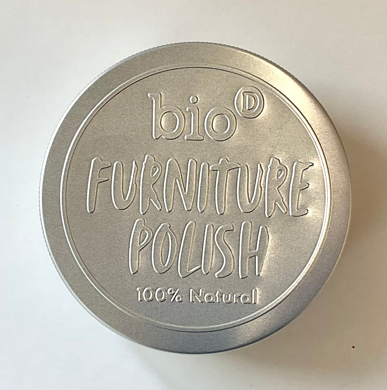 Metallic container lid with 'bio-d Furniture Polish 100% Natural' text on a white background