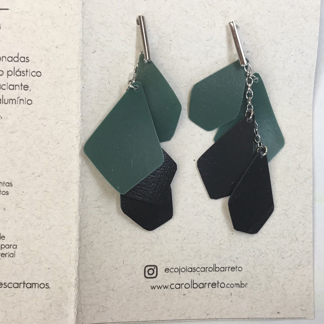 A pair of earrings made from recycled shampoo bottles, presented on a cardboard holder with the brand name 'World Design Carol Barreto'.