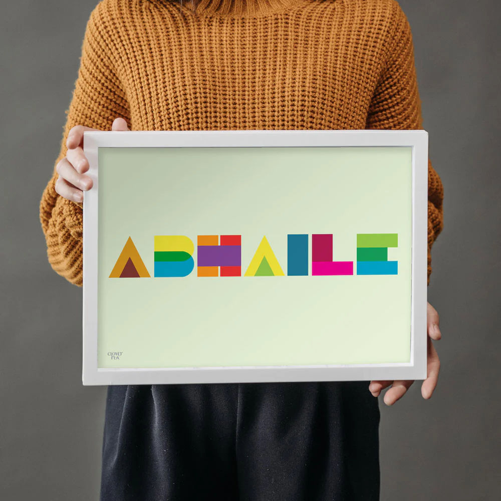Person holding a framed colourful text art piece "Abhaile".