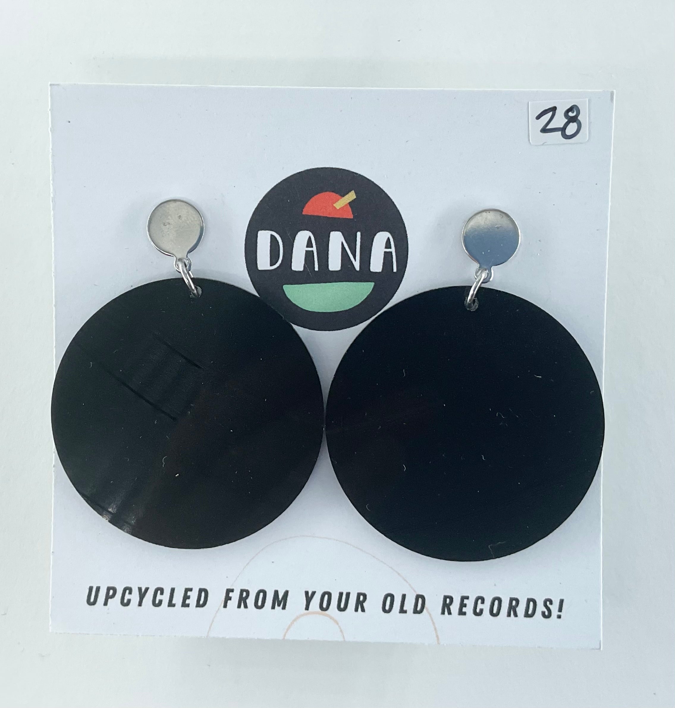 Black round earrings on a Dana brand card with text about upcycling from old records.