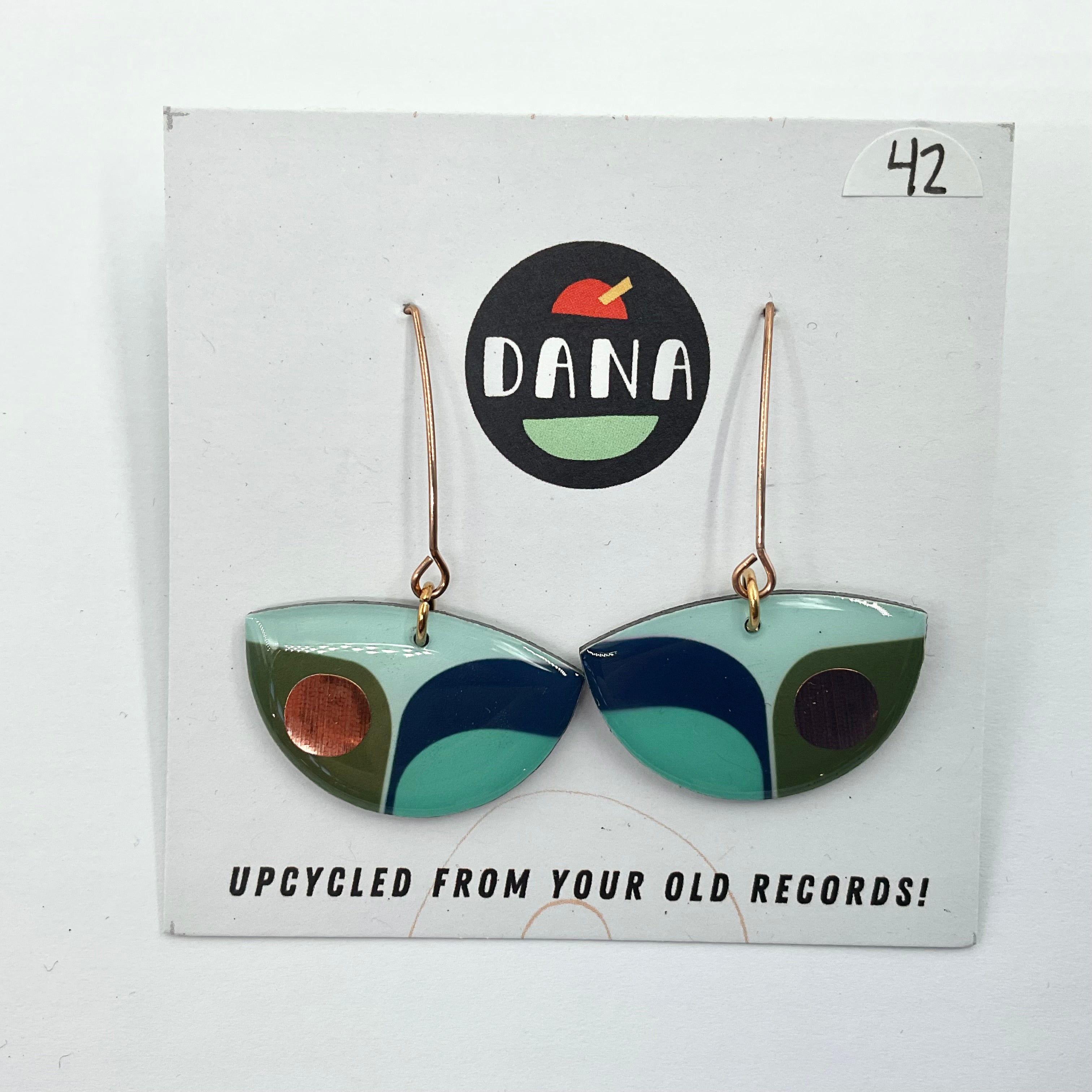 A pair of green boat-shaped earrings made from upcycled vinyl records, displayed on a white card with the Dana brand logo.
