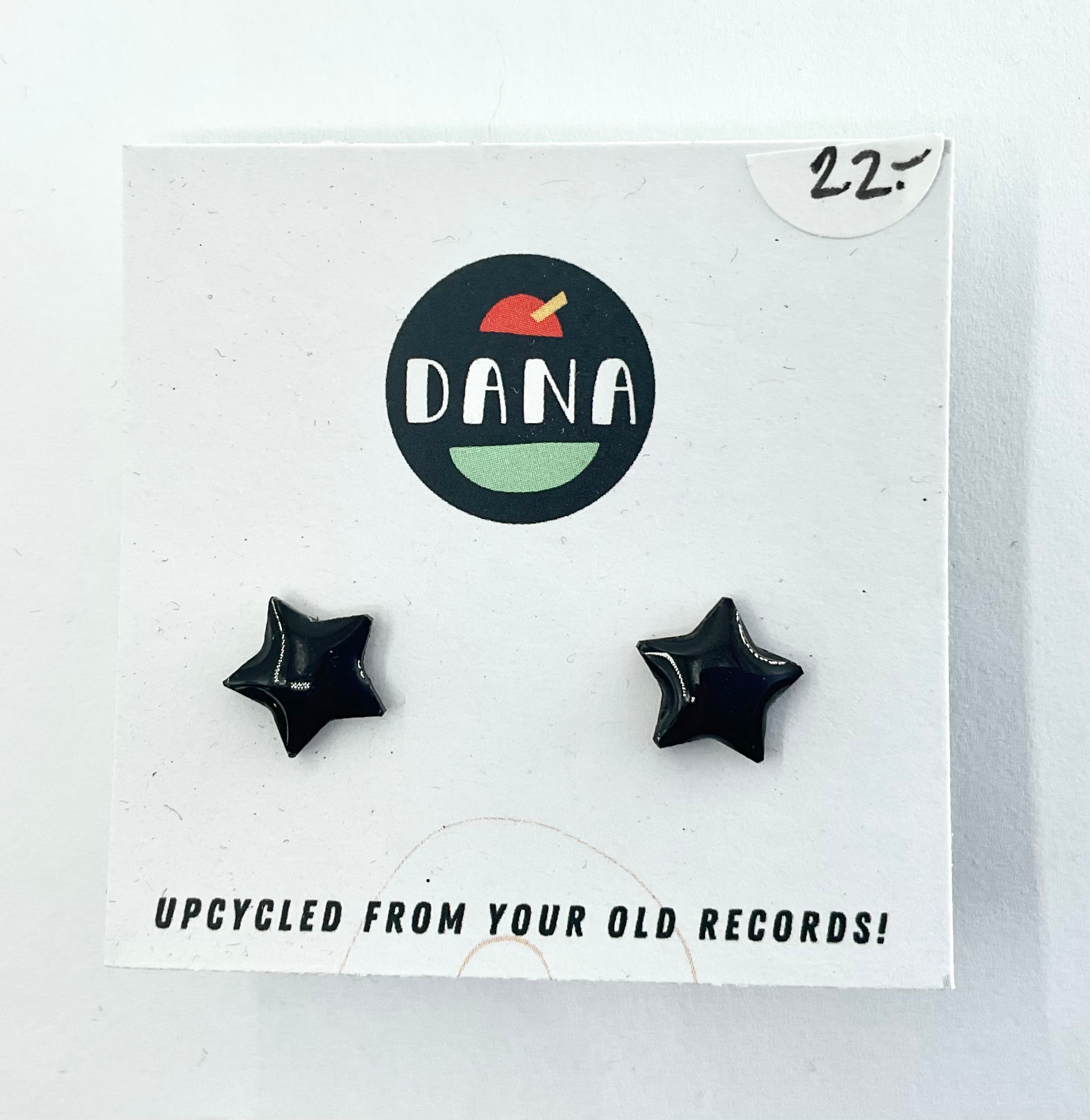 A pair of black star-shaped stud earrings on a white card with the brand name 'DANA' at the top. The card indicates the earrings are made from upcycled vinyl record jewellery.