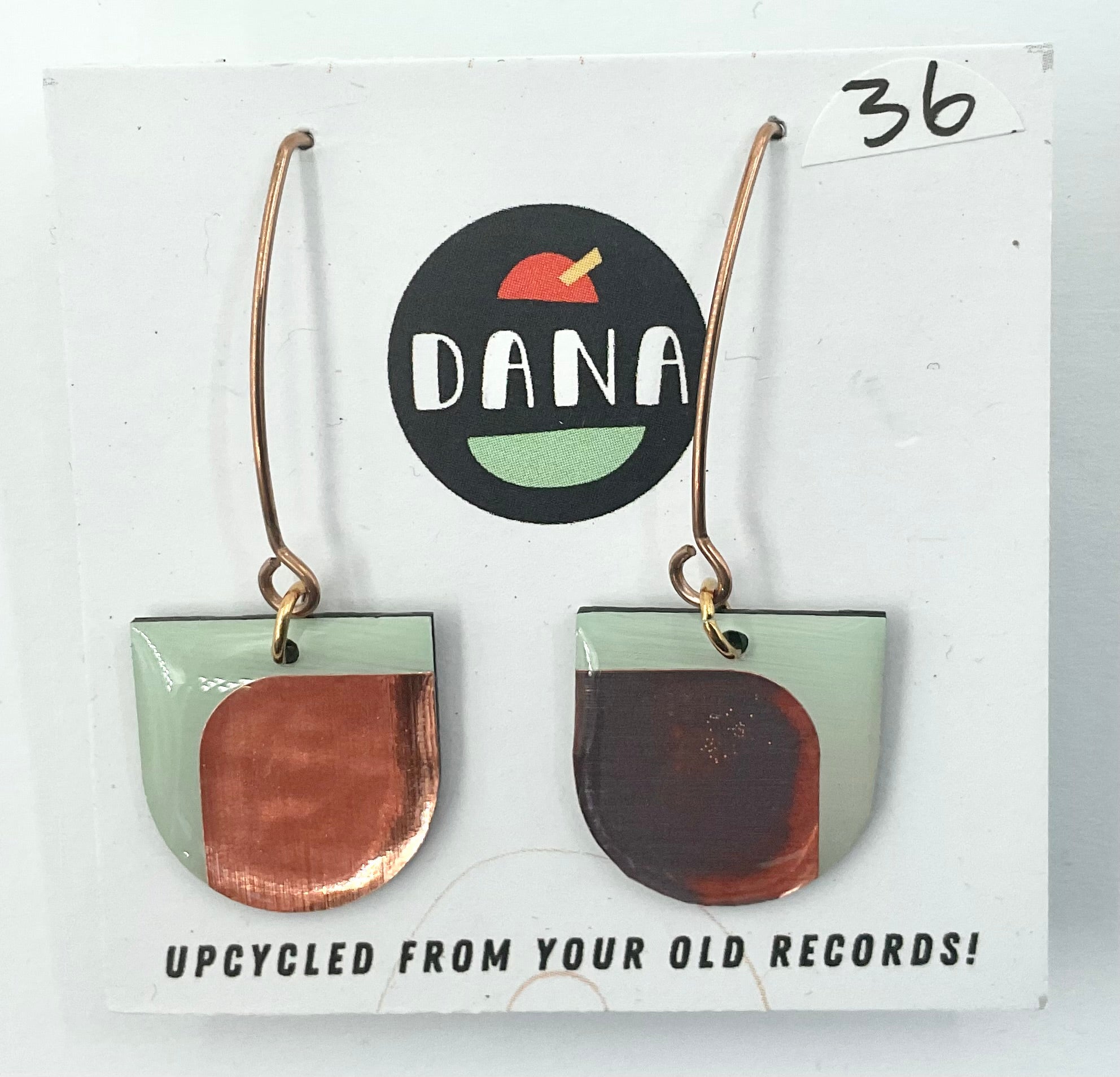 A pair of green and metallic details earrings, with the brand name Dana displayed on the packaging, indicating they are upcycled from old records.