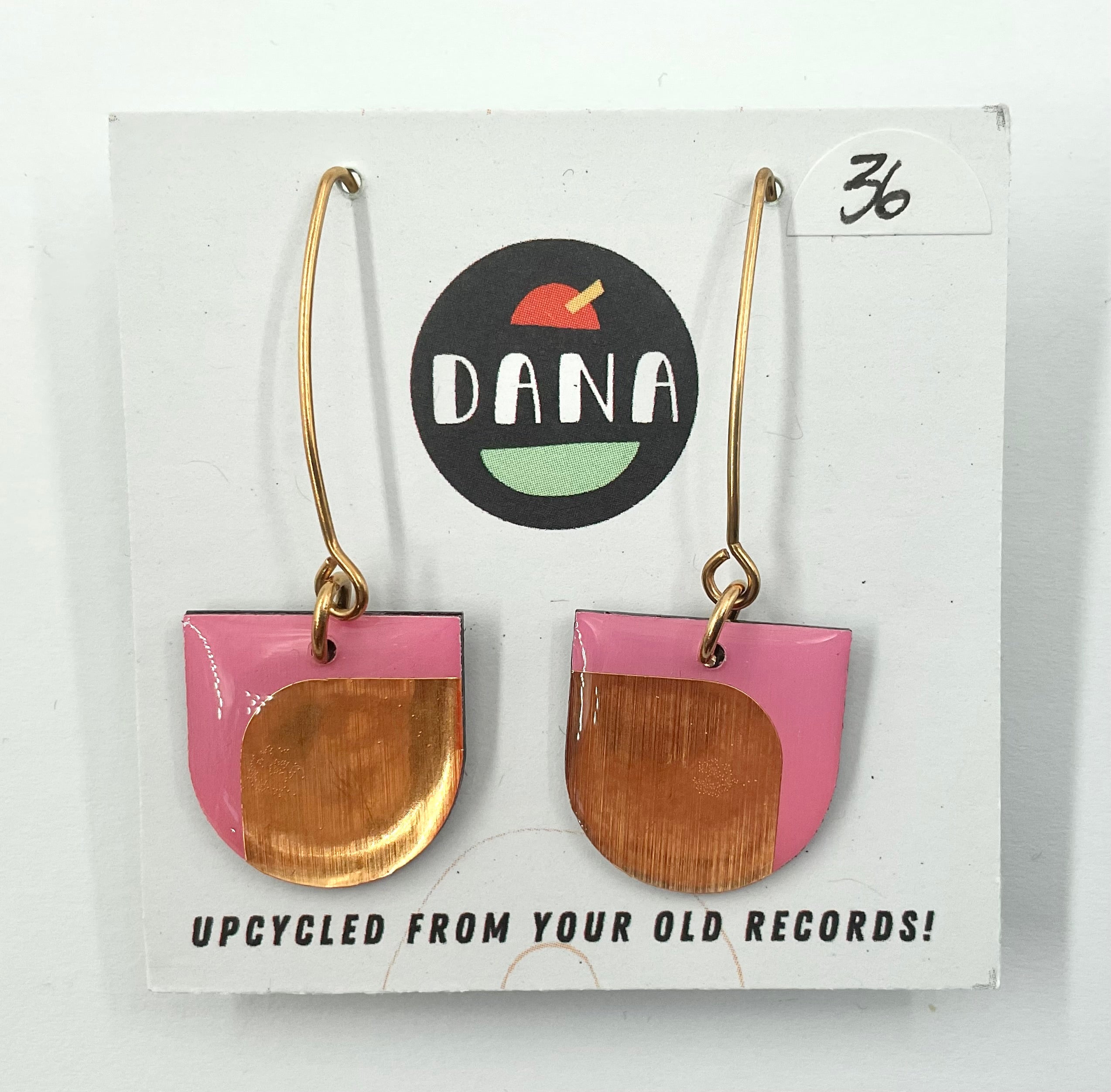 A pair of Dana Jewellery Dee earrings, small arches with metallic details, displayed on a card indicating they are upcycled from old records.