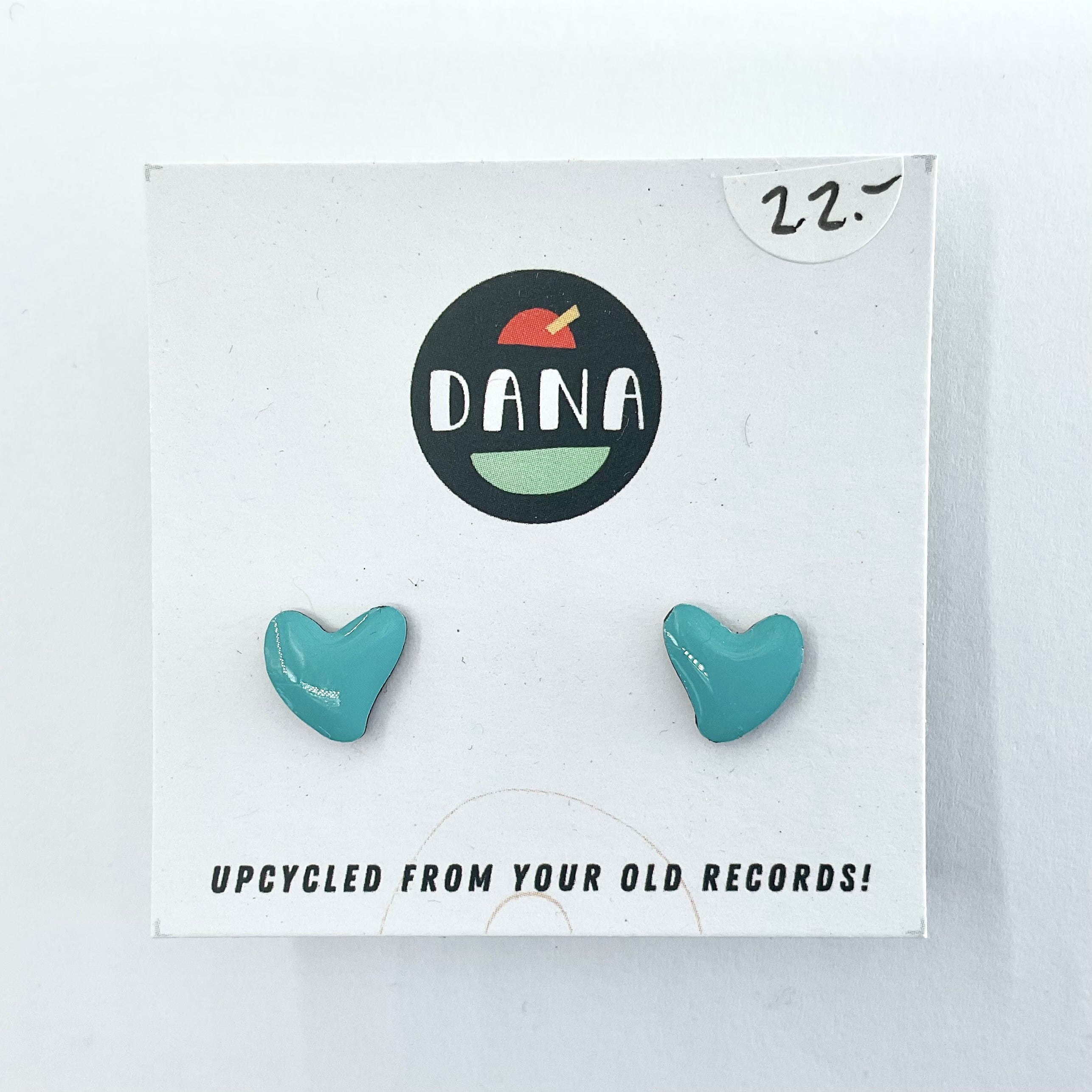 A pair of green heart-shaped stud earrings on a white card with the brand name 'dana' displayed at the top. The earrings are described as upcycled from old records.
