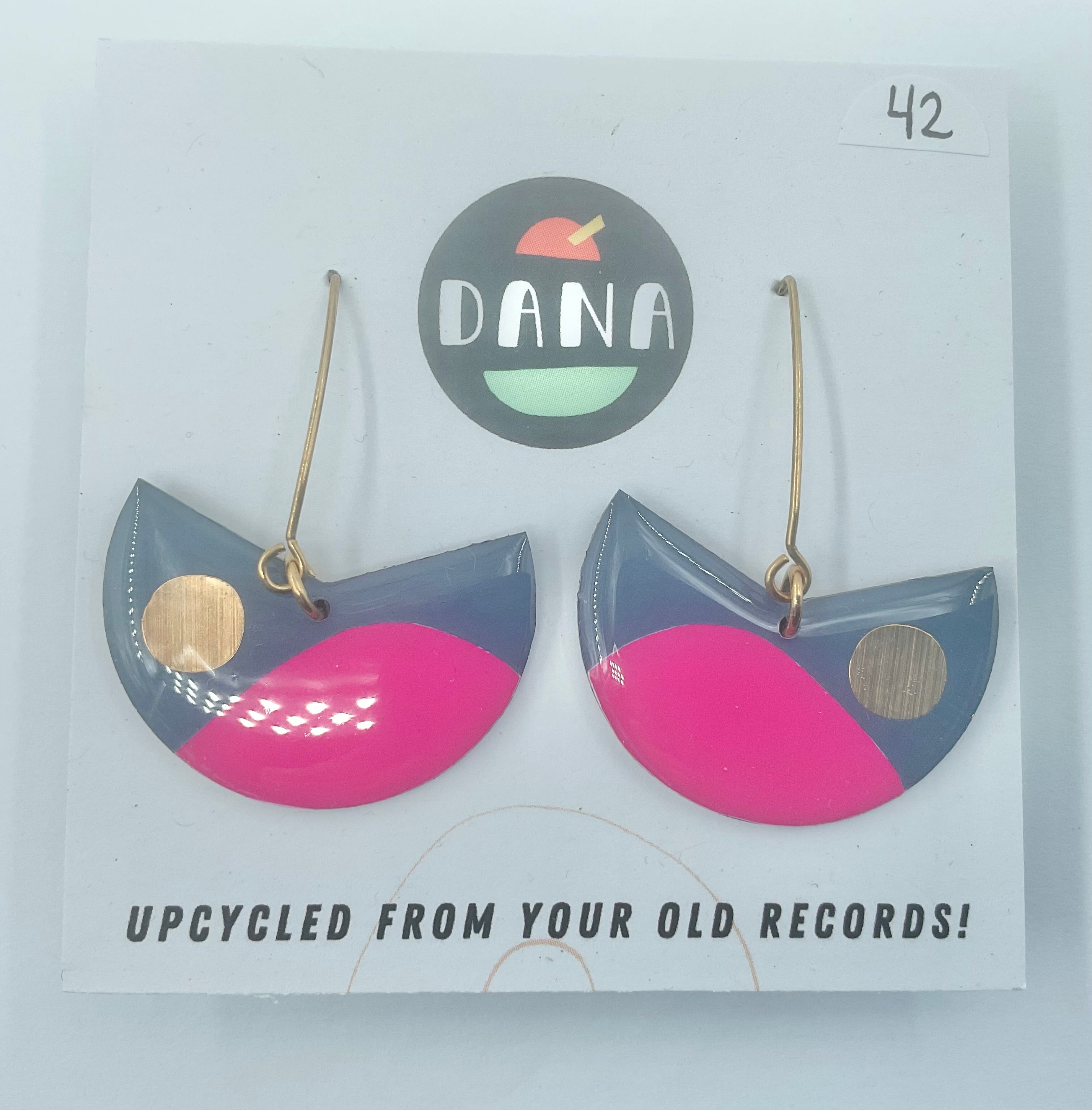A pair of Pacman earrings in grey, fuschia, and gold colors, displayed on a card with the brand name Dana.