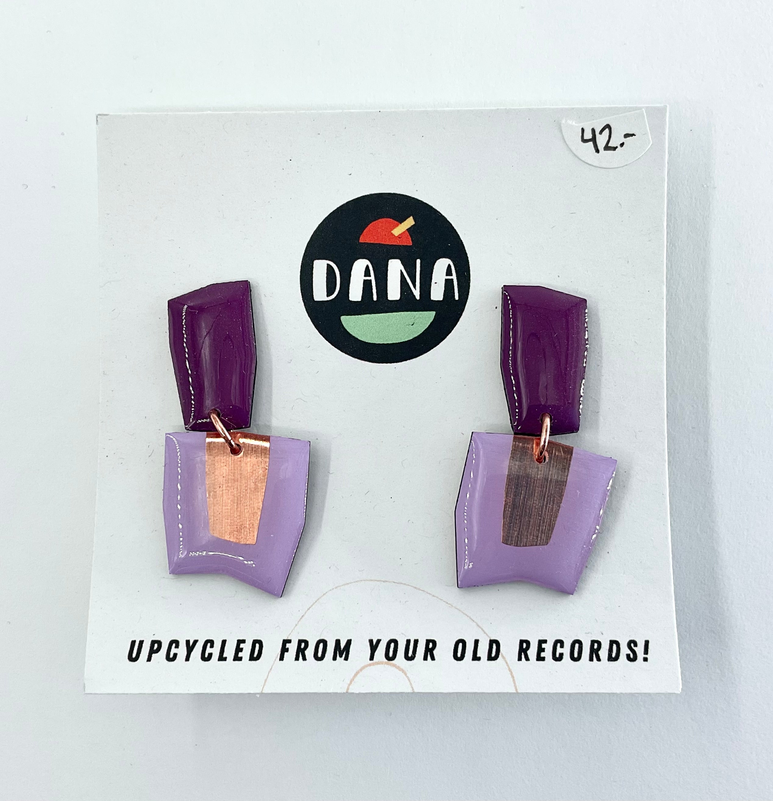 A pair of purple earrings made from upcycled vinyl records, displayed on a white card with the brand name 'DANA' at the top.