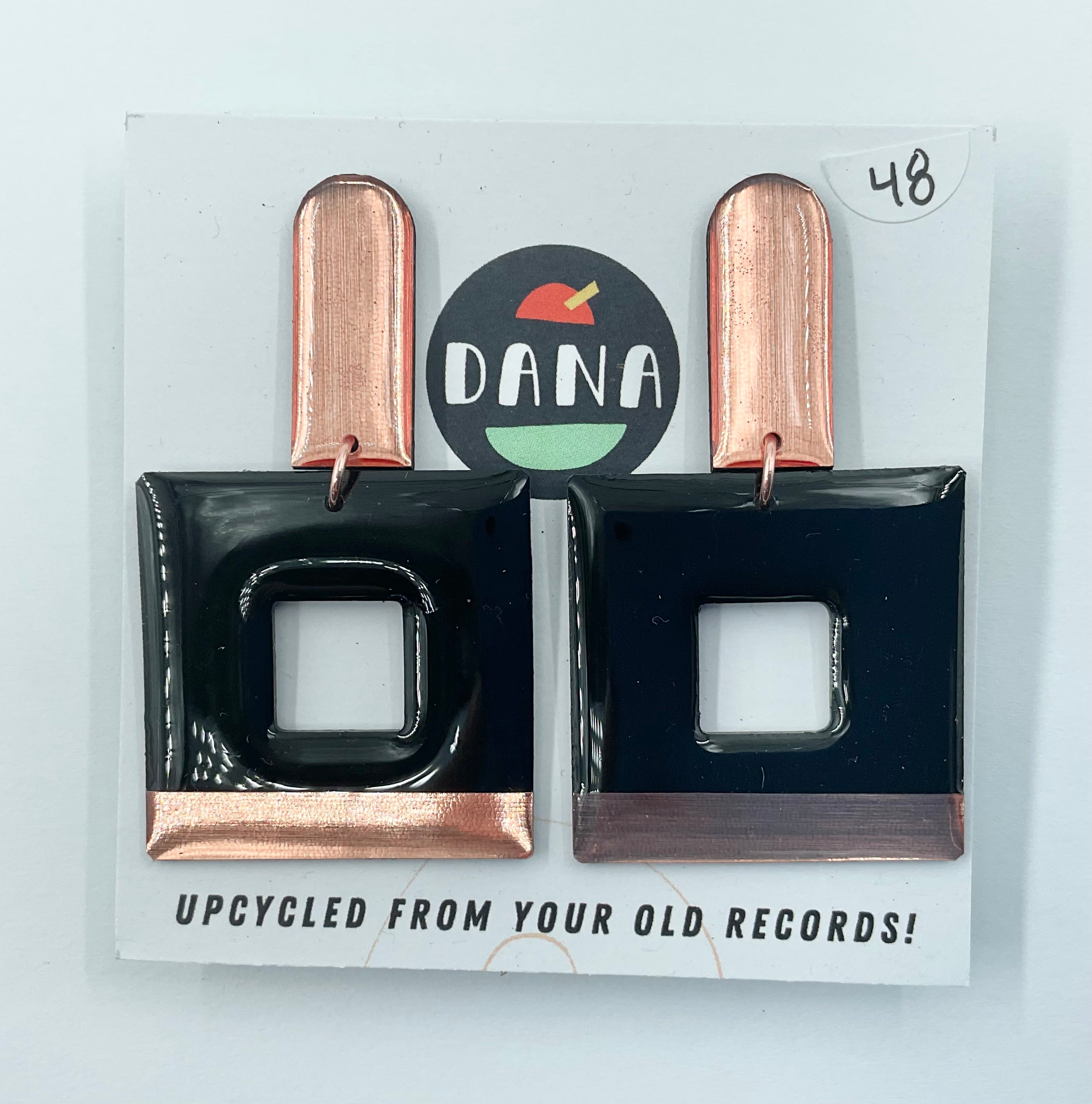 A pair of Dana Jewellery Mika earrings in black and copper, displayed on a card indicating they are upcycled from old records.
