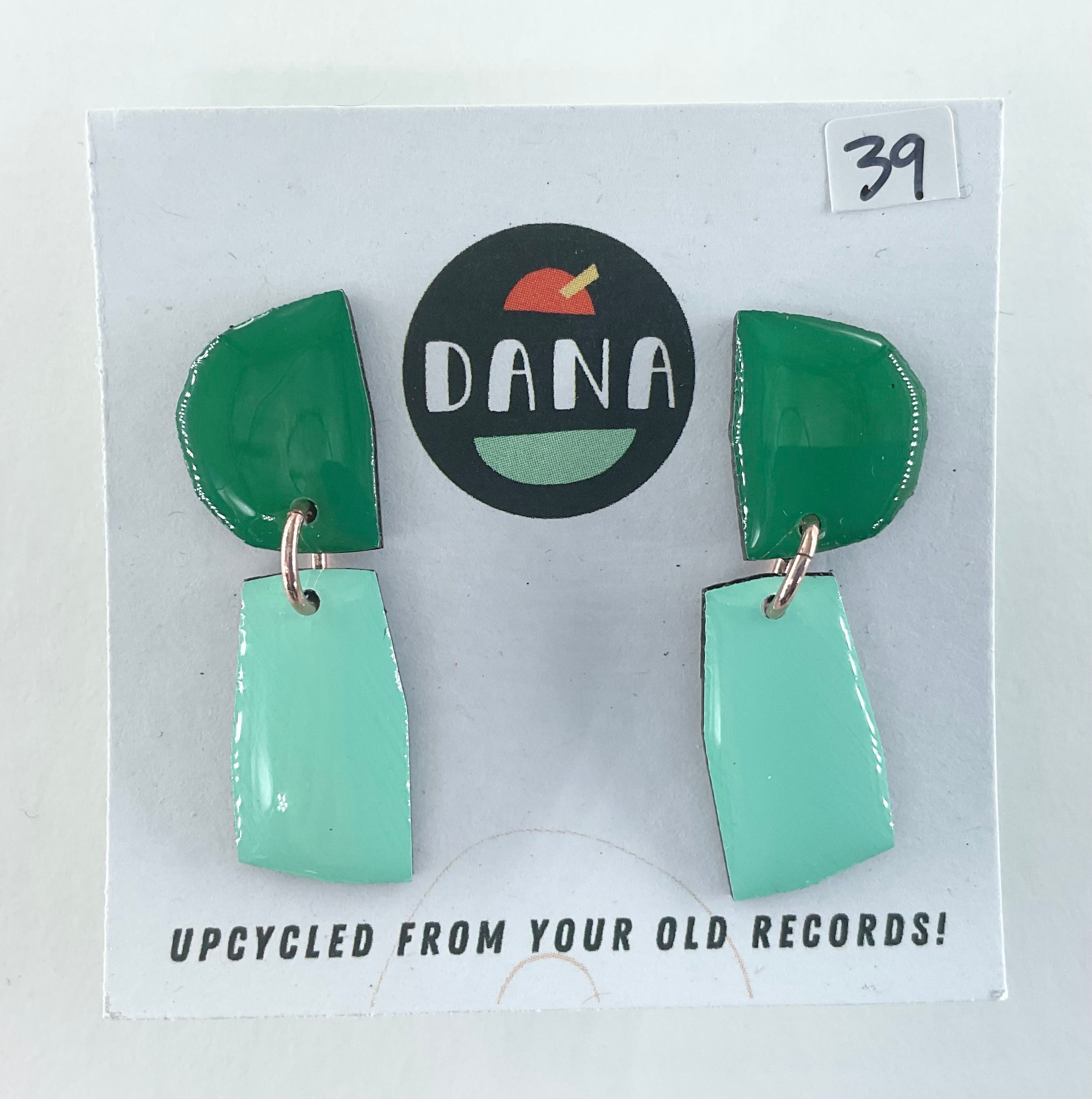 Green and teal earrings on a card with 'DANA' branding and text about upcycling from old records.