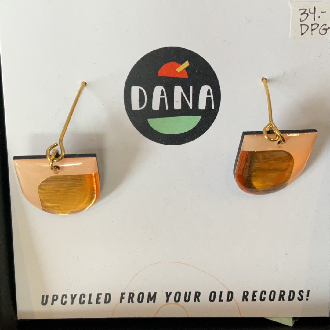 A pair of bronze-colored earrings with a textured surface, displayed on a cardboard stand with the brand name 'Dana' and a logo featuring an apple and a boombox.