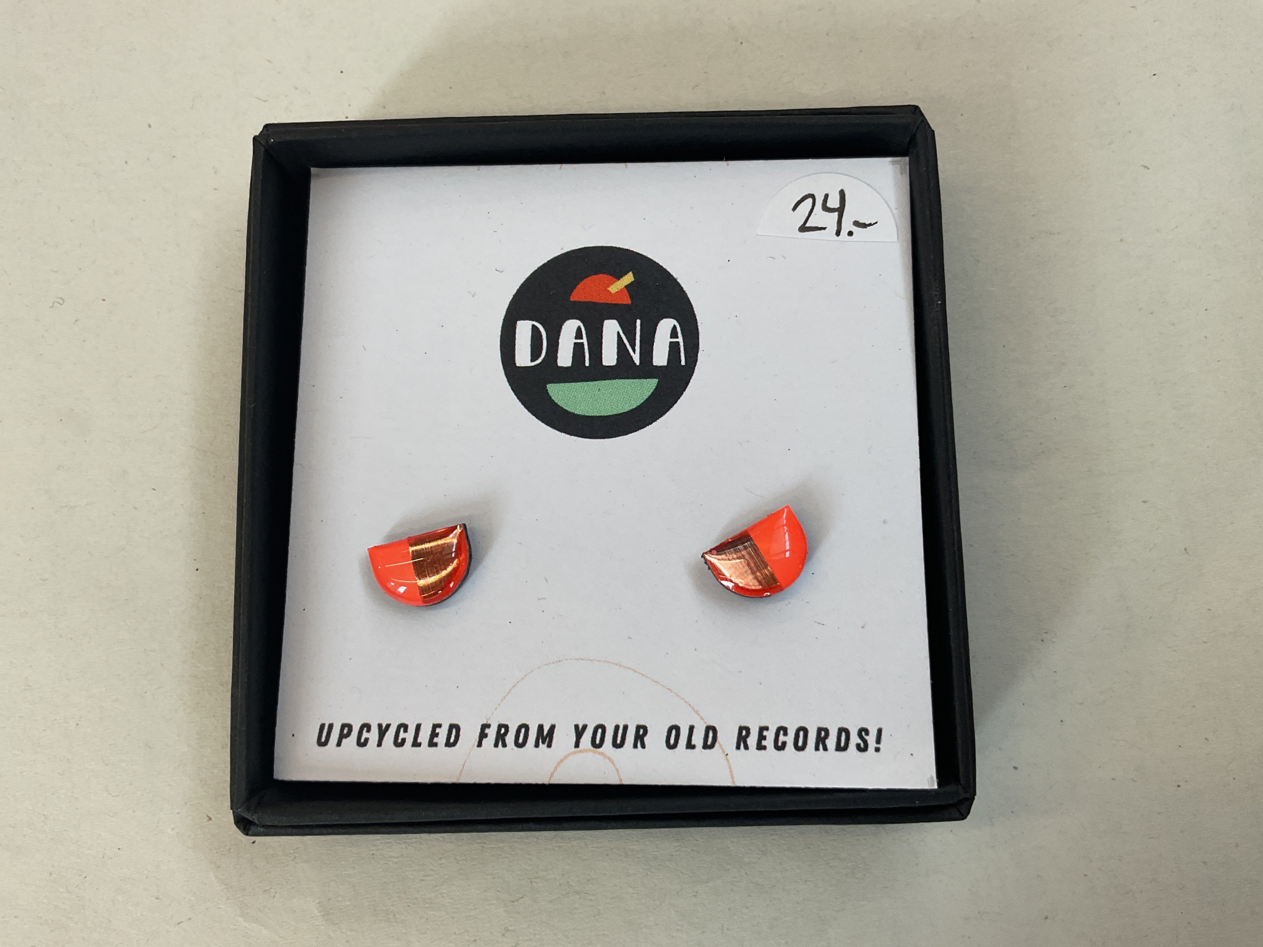 A pair of orange earrings made from upcycled vinyl records, presented in a black box with the Dana Jewellery logo.