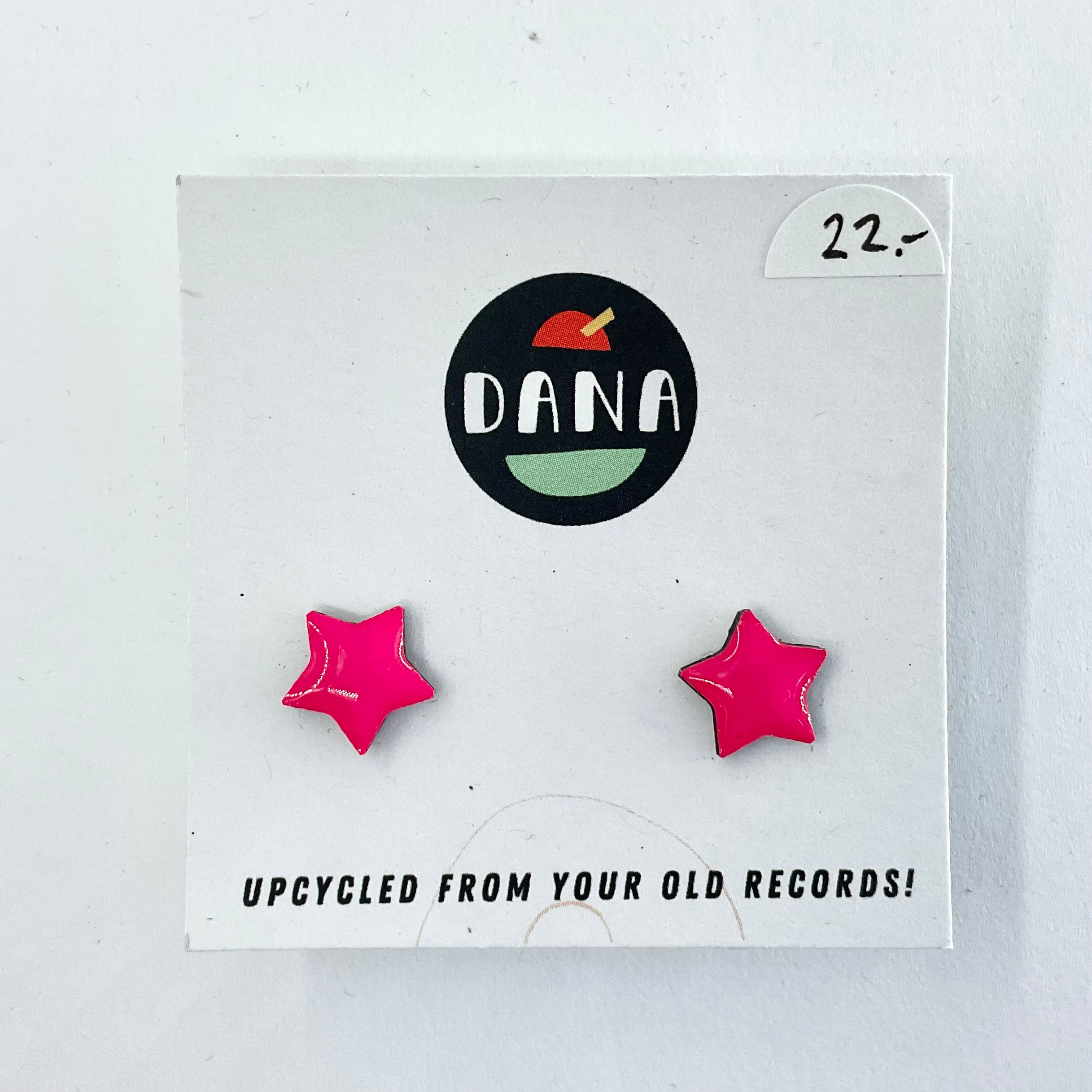 A pair of pink star-shaped stud earrings on a white card with the brand name 'dana' at the top. The card has the text 'upcycled from your old records!'