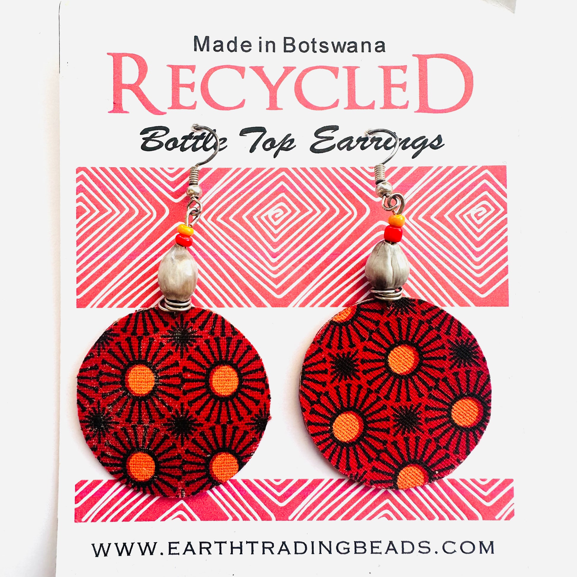 A pair of recycled bottle top earrings with pink, orange, and black geometric patterns, displayed on a card with 'Made in Botswana' text and the brand name 'Earth Trading'.