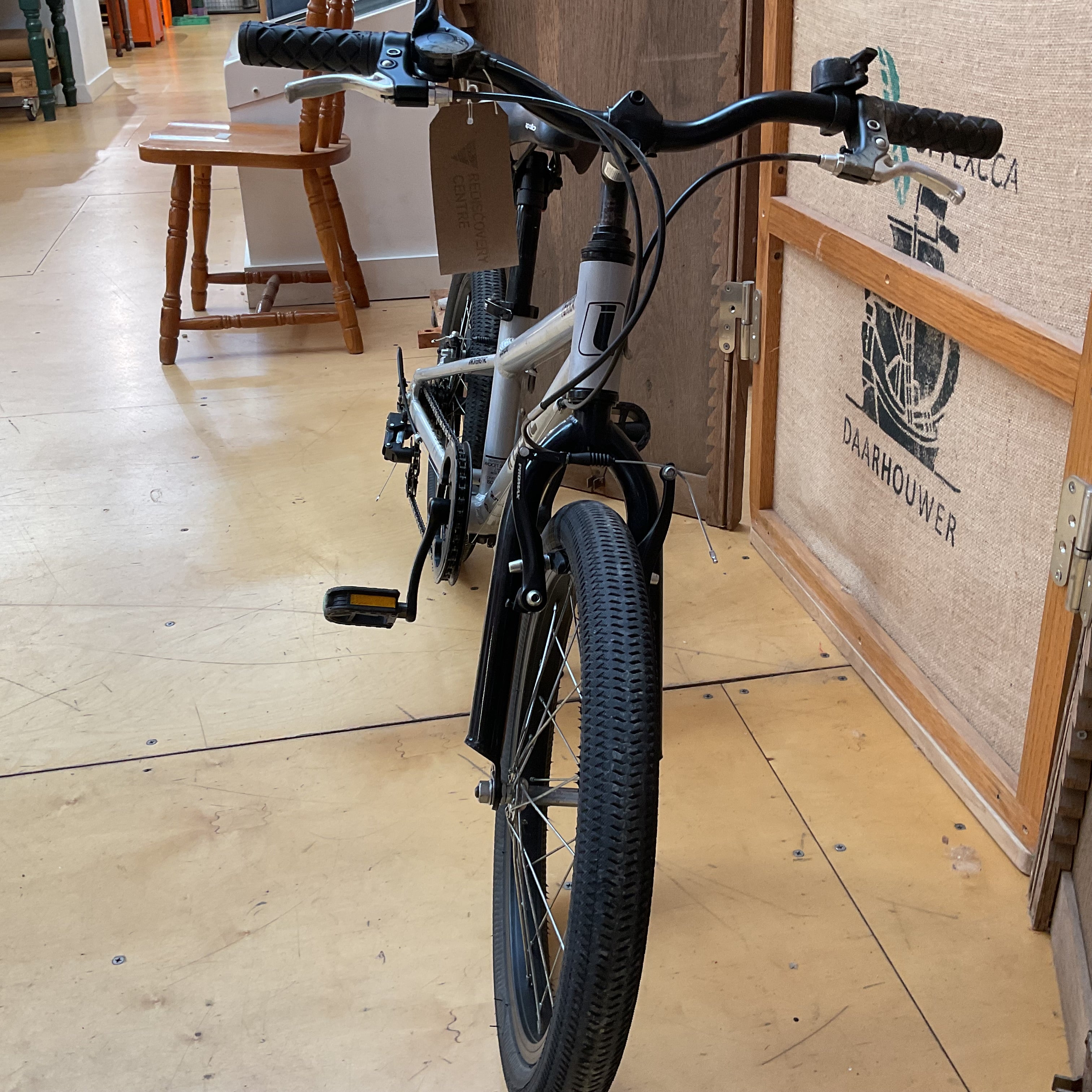 A black and white step-through bicycle with a front fender and rear rack, photographed indoors on a wooden floor next to a wooden crate.