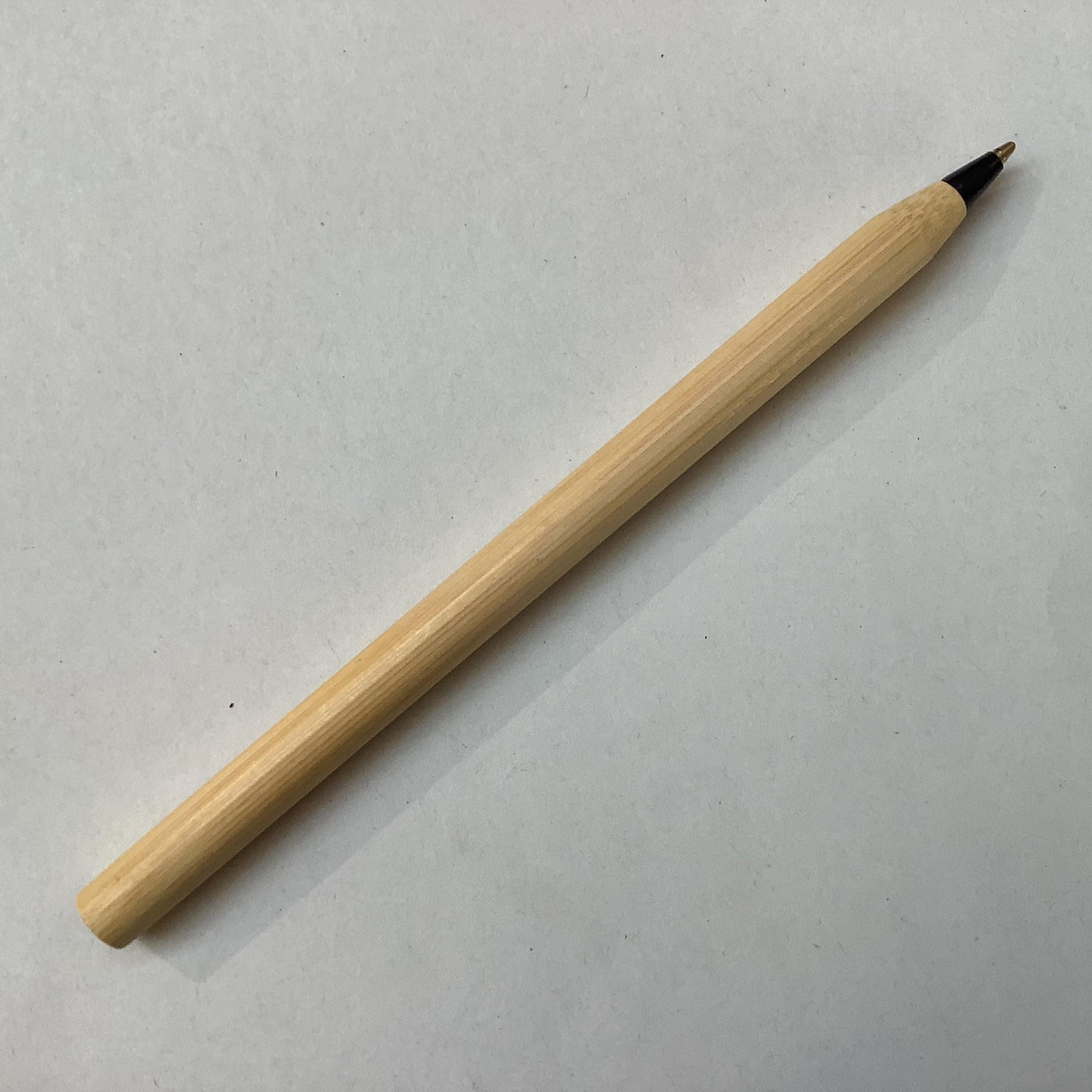A light natural bamboo pen with a black and gold tip, placed diagonally on a plain light gray surface.