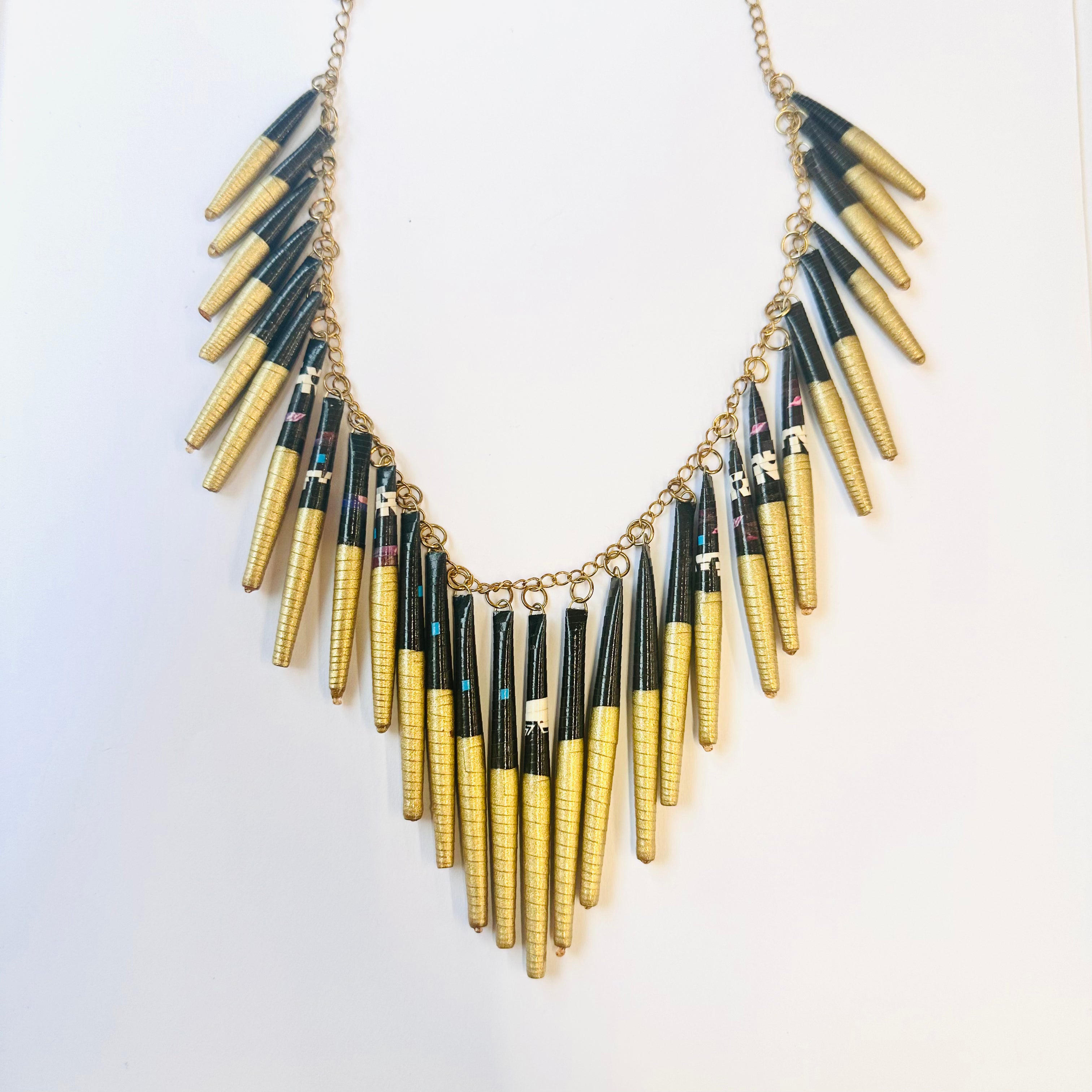 A beaded necklace with a mix of gold, black, and beige colors, made from recycled magazine paper.