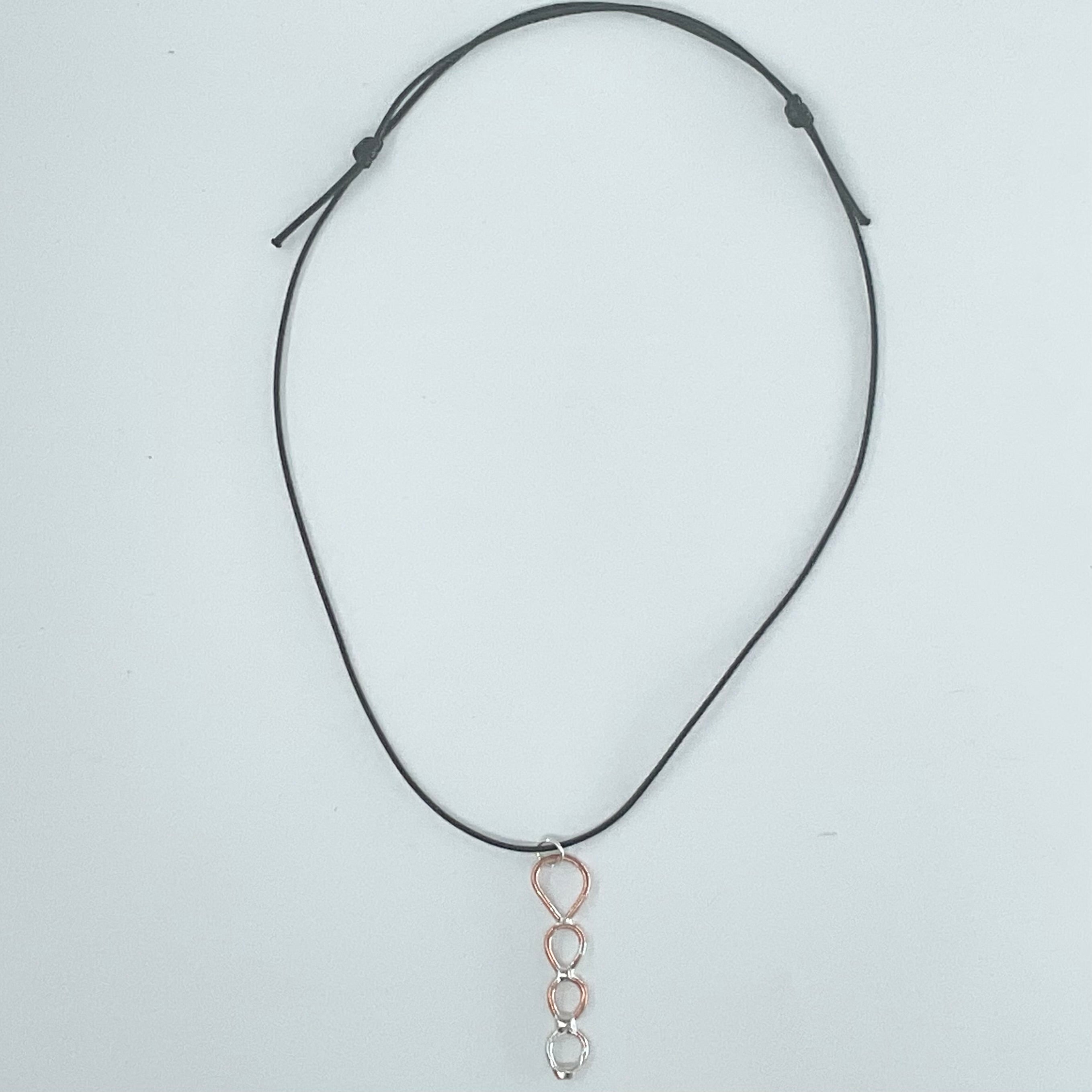 A black adjustable cord necklace featuring a dangling pendant with a rose gold teardrop frame and three silver-toned oval links at the bottom, displayed on a light gray background.