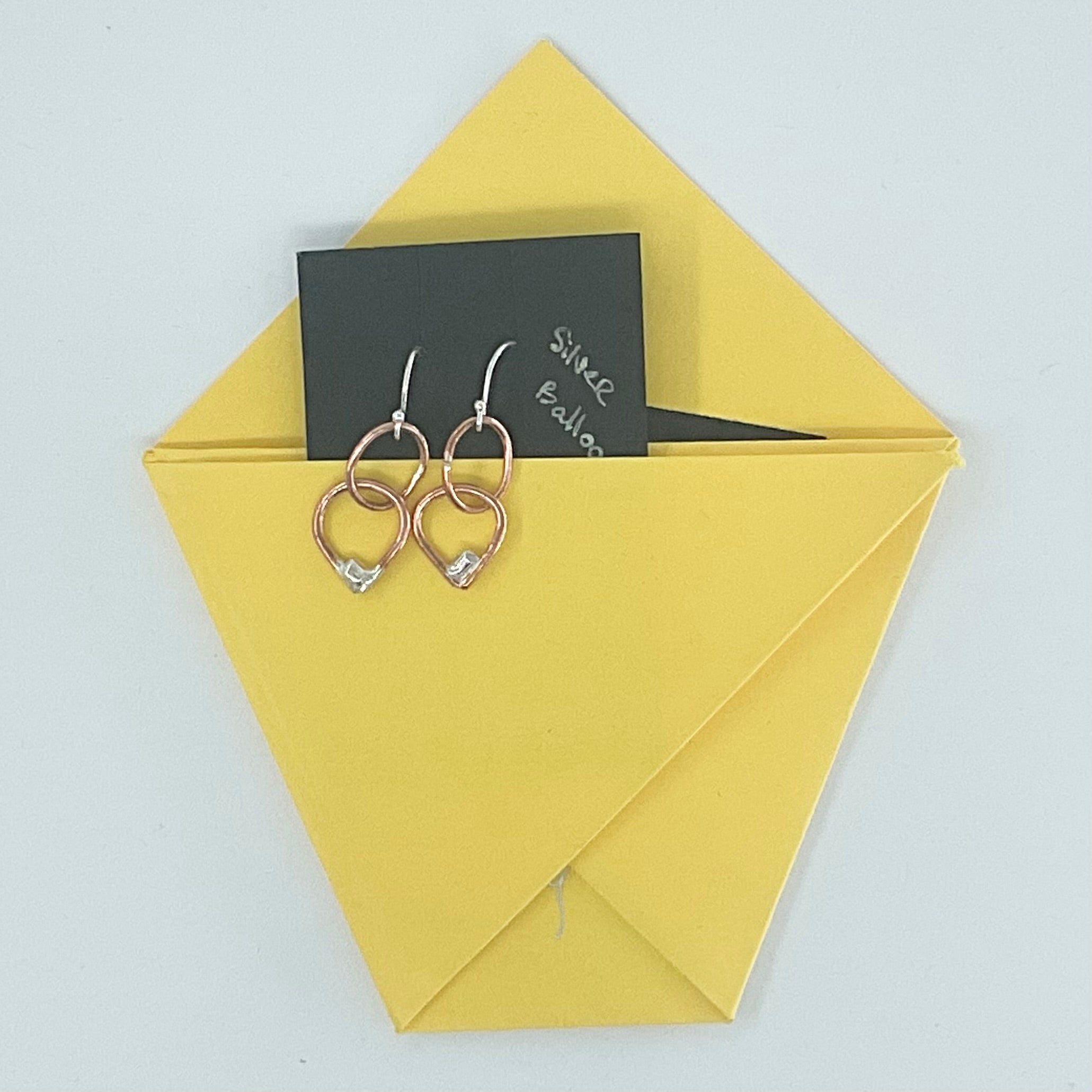 A pair of rose gold double hoop earrings with small clear crystal accents, presented on a yellow envelope with a black card that reads 'Since 2020'.