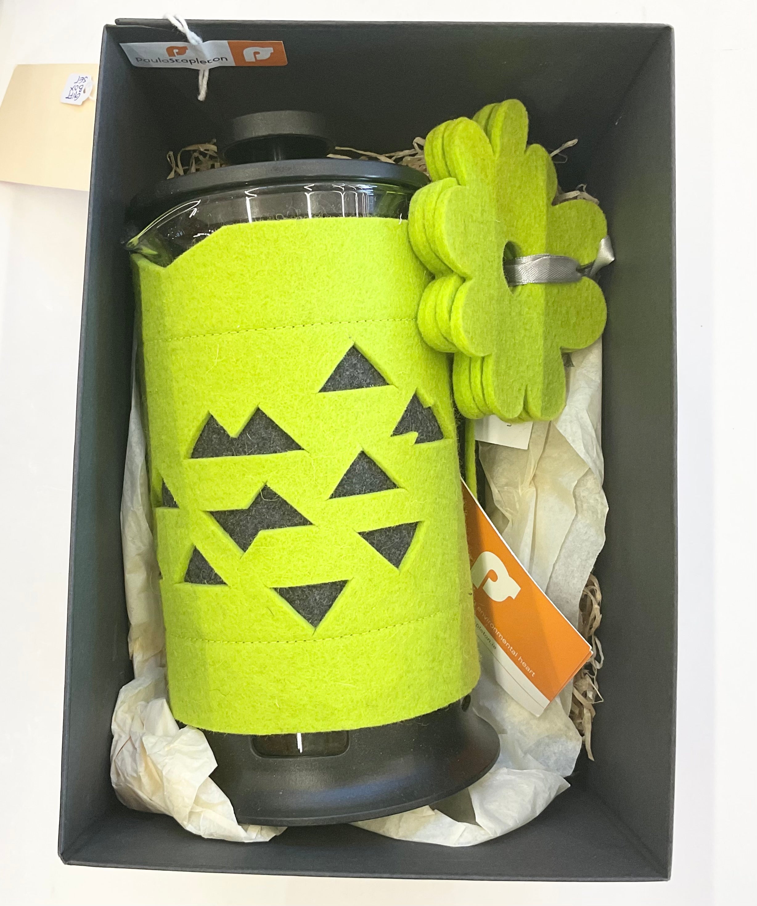 Green geometric-patterned Cafetiere holder with 3 flower shaped coasters inside a black box on paper packaging