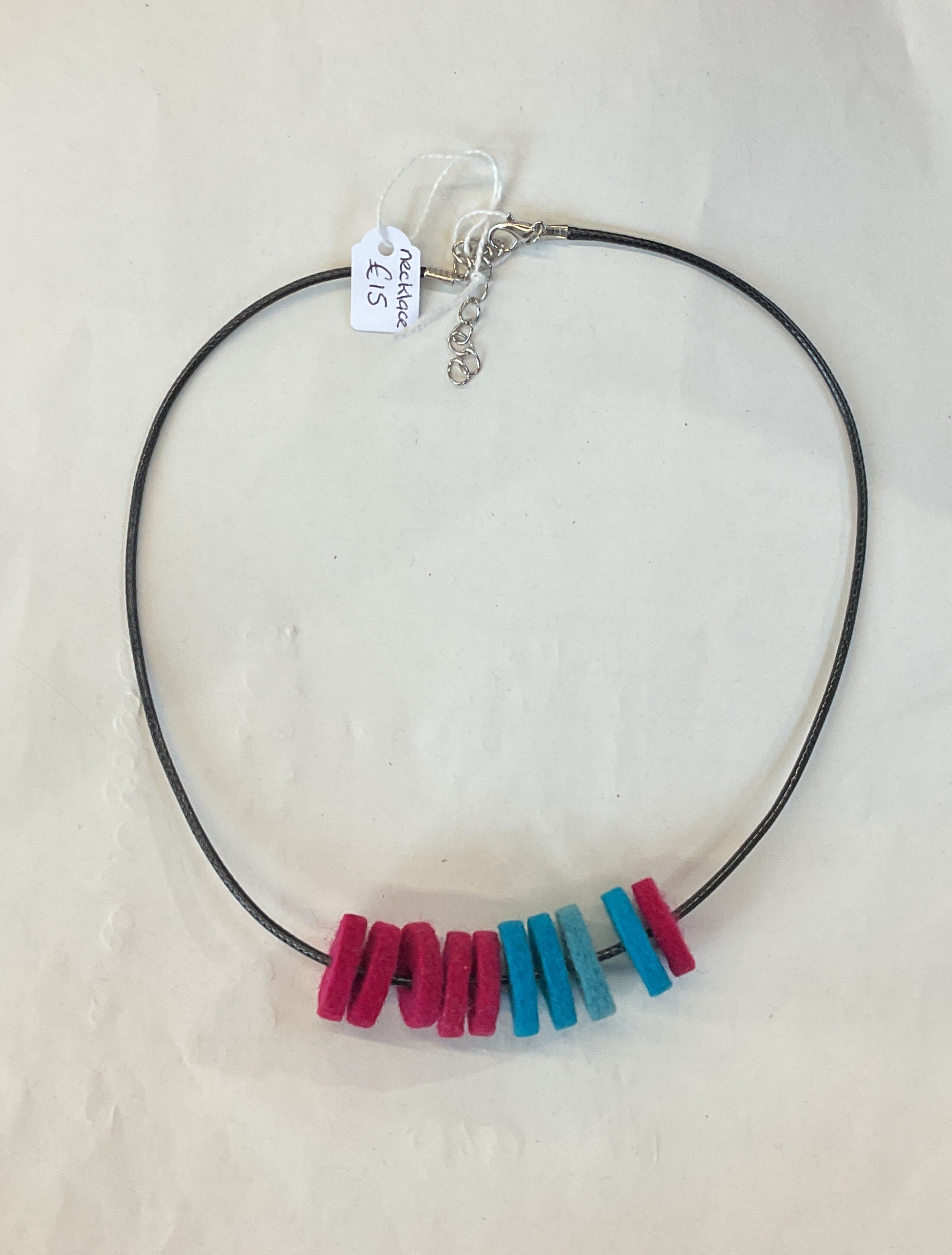 Necklace with colorful felt beads on a black cord against a white background