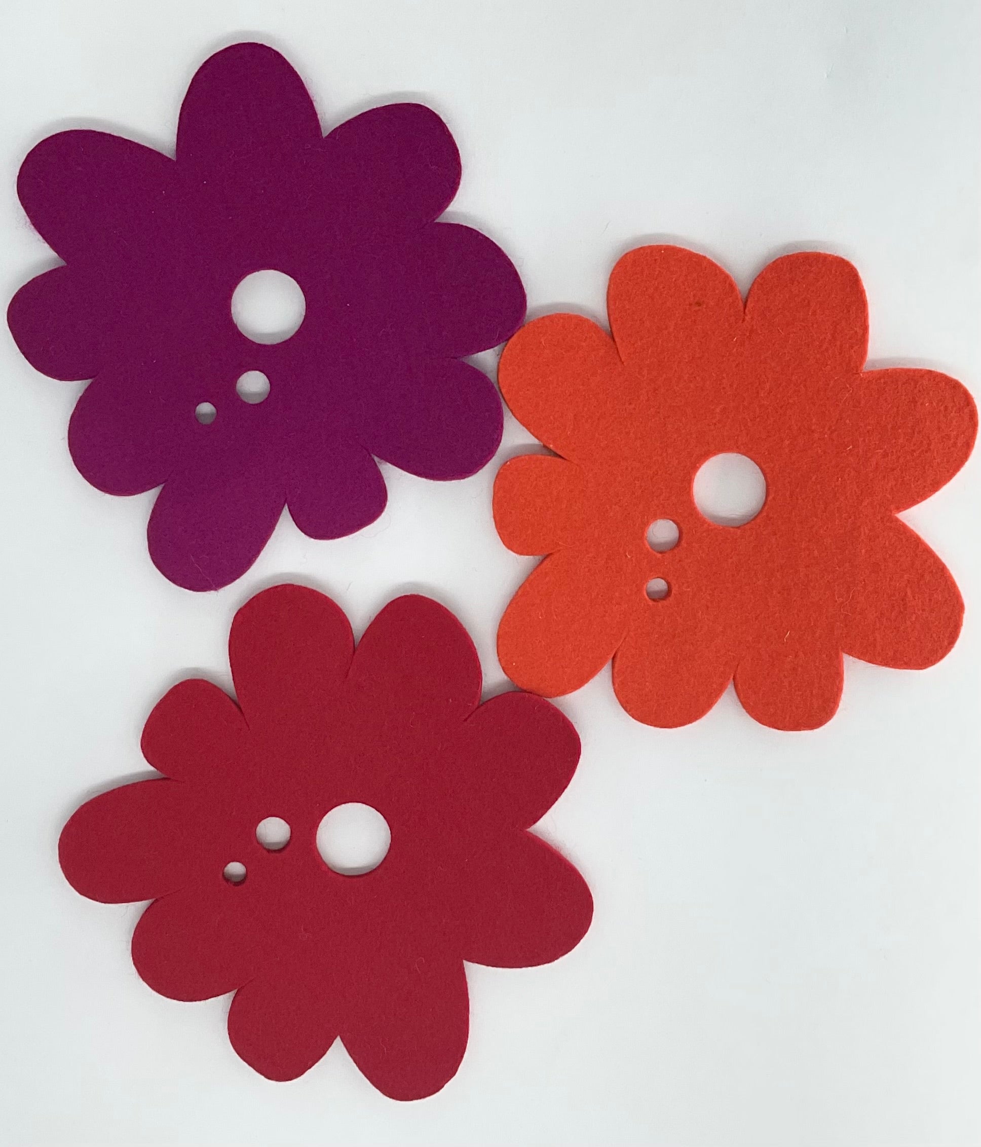 Three flower-shaped pot stands in purple, red, and orange on a white background