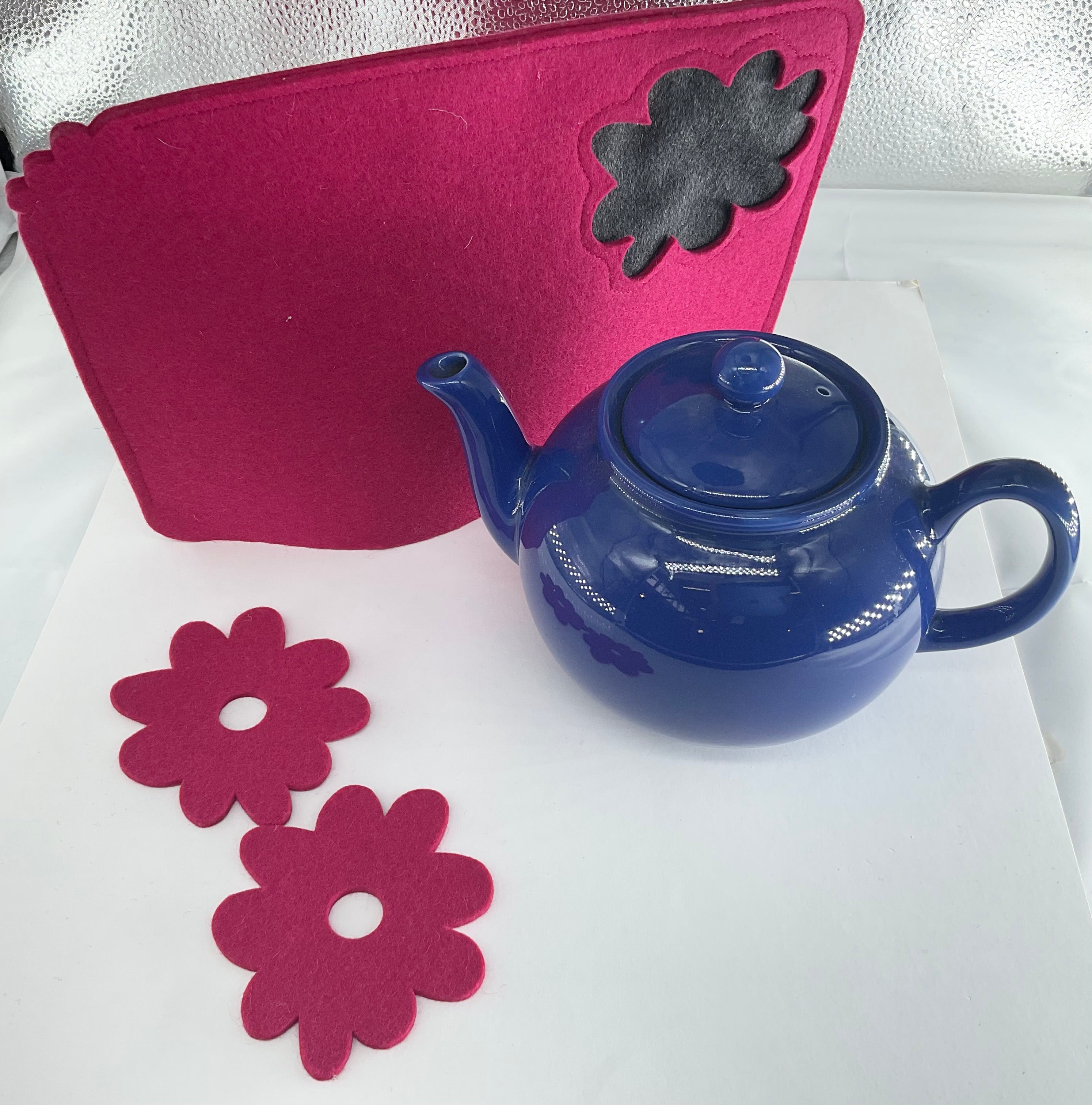 Blue teapot with pink flower-shaped coasters and a teacosy on a white surface