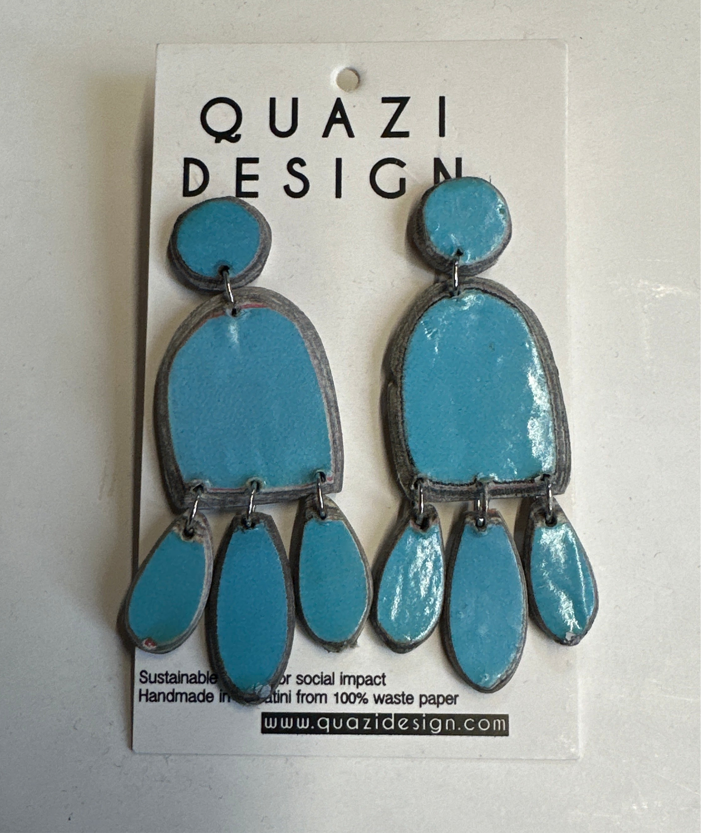 Blue earrings on a Quazi Design card with branding and sustainability information.