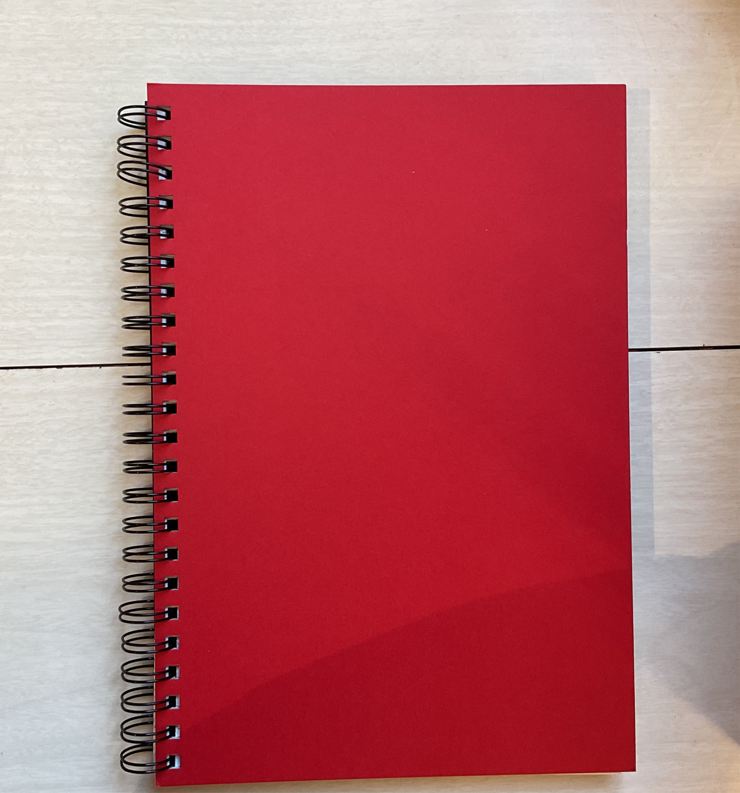 A red hardcover notebook with a wire binding, A4 size, lying flat on a surface.