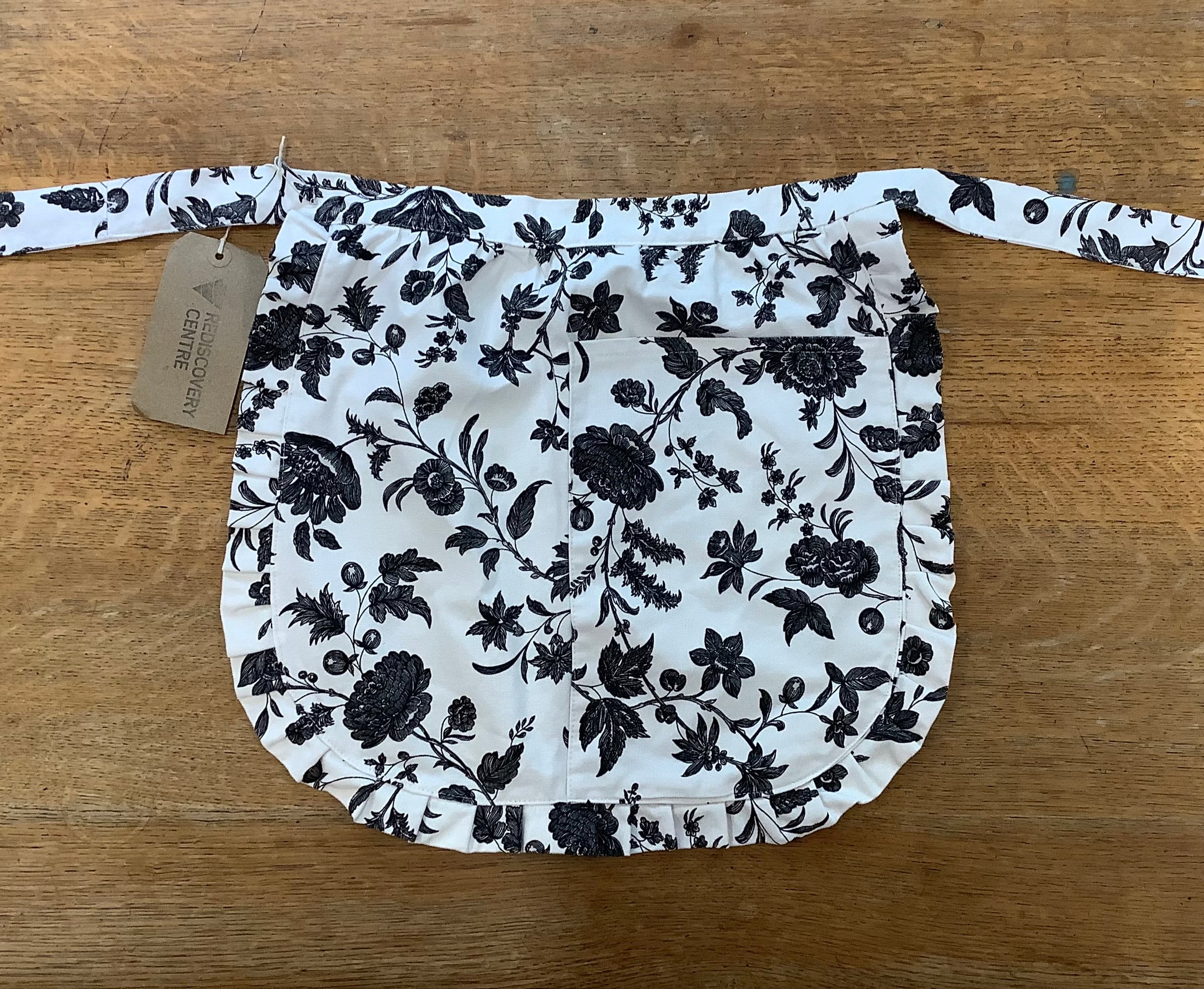 Floral-patterned apron on a wooden surface with a visible brand tag.