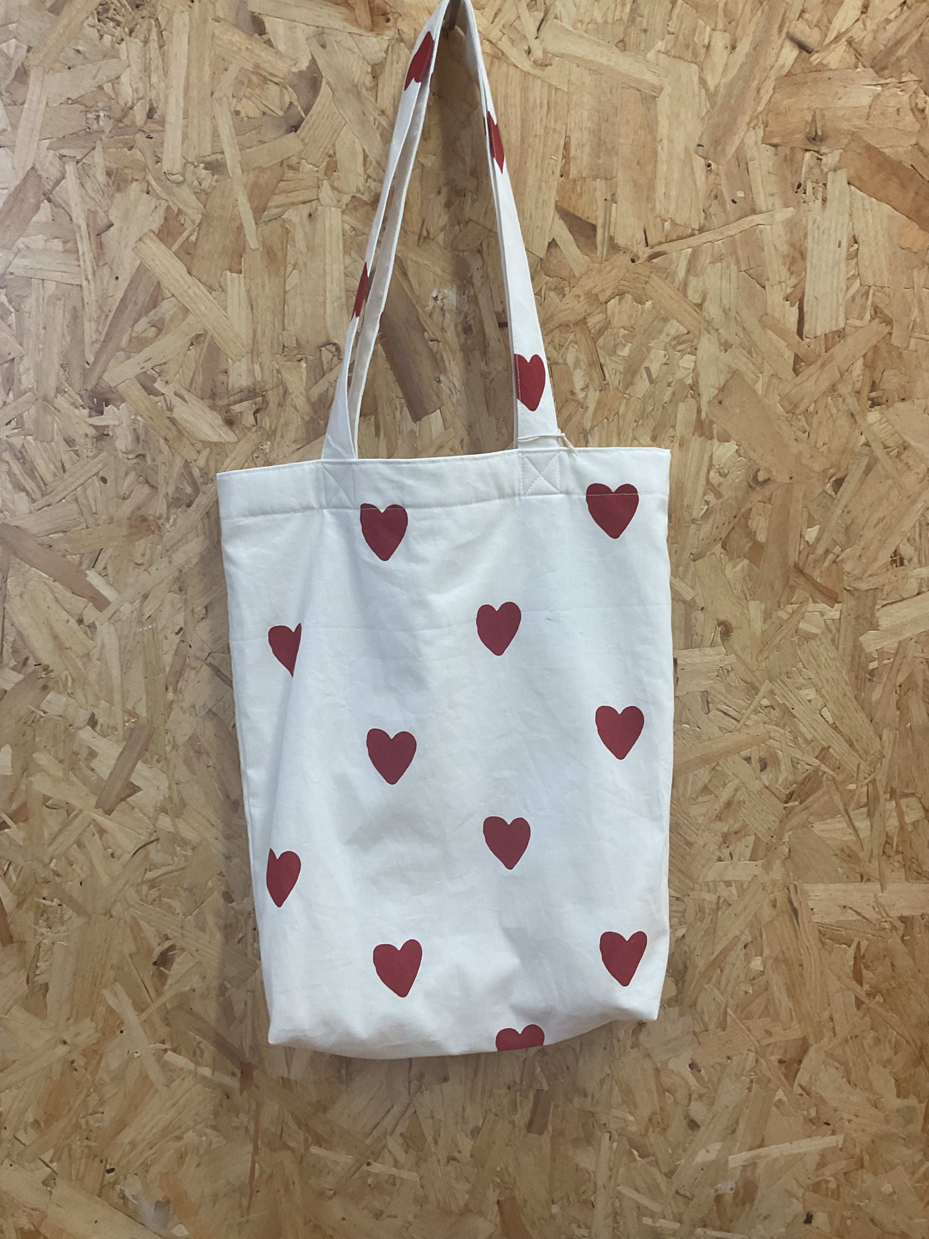 White tote bag with red heart patterns on a wooden floor