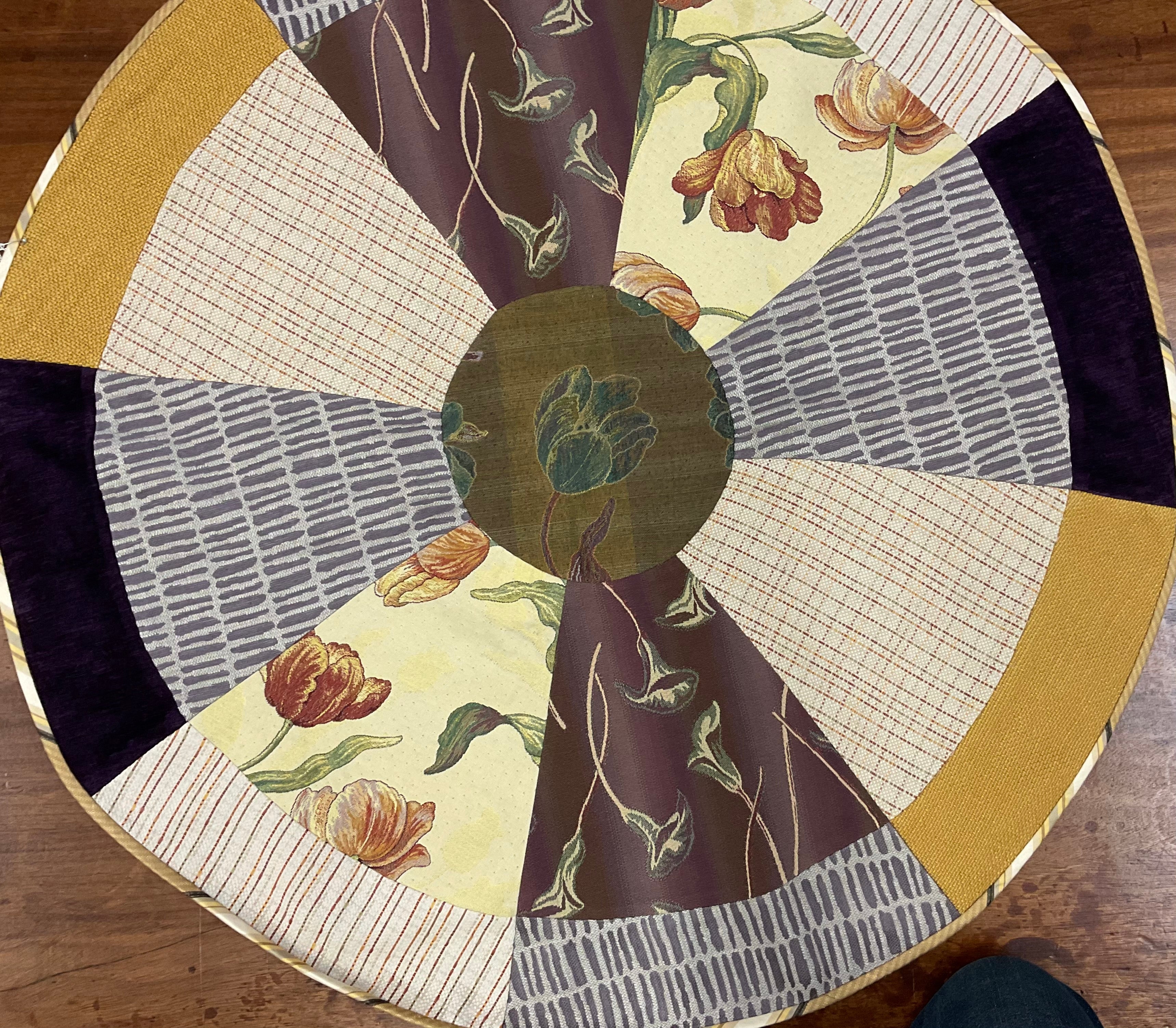 Round table with a patchwork design featuring floral and geometric patterns on a wooden floor.
