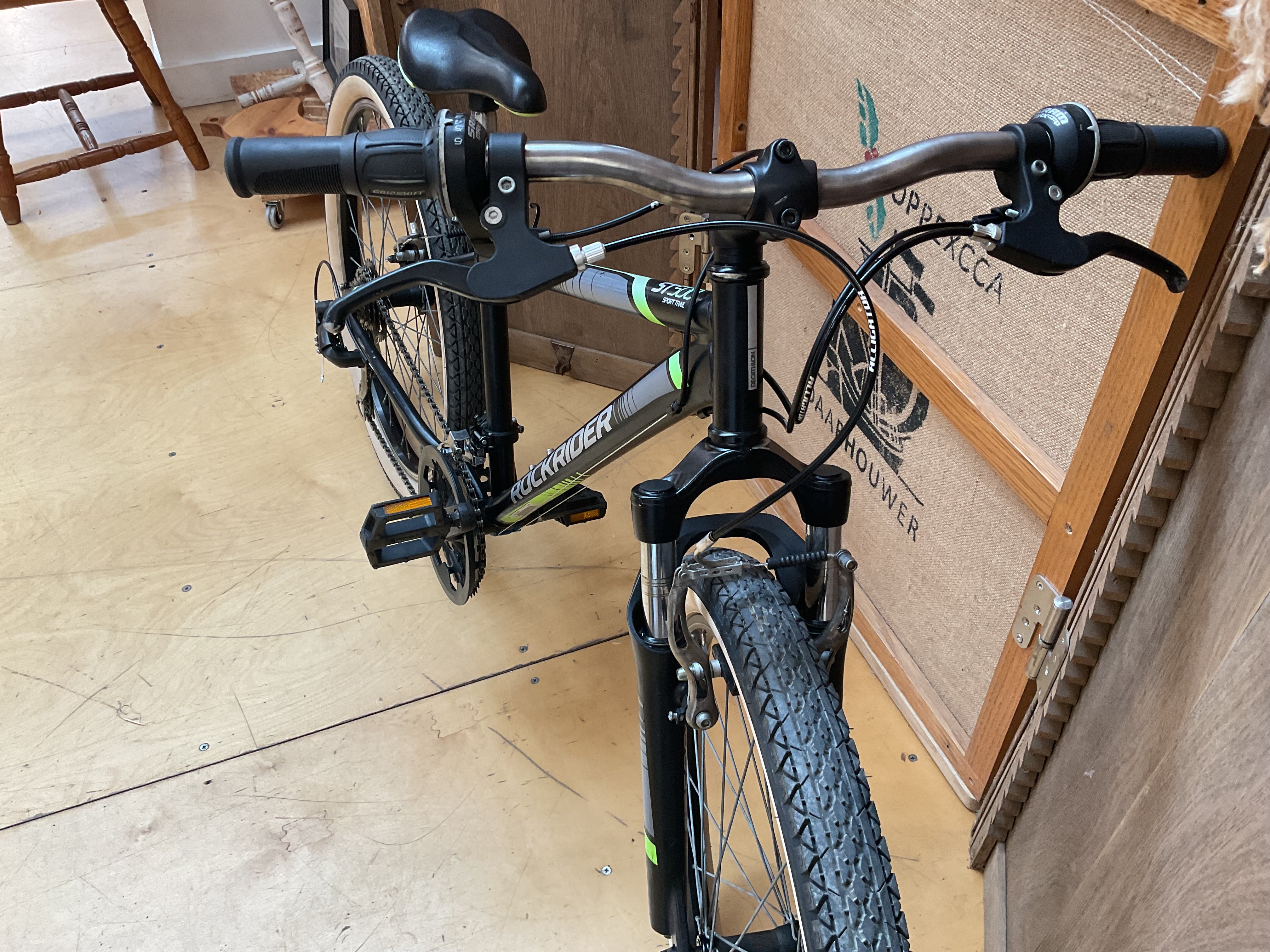 A black and silver mountain bike with a front suspension fork, black handlebars, and a black saddle, photographed indoors against a cardboard shipping box.
