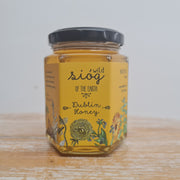 A jar of Sióg of the Earth Honey displayed on a wooden surface with a decorative label featuring botanical illustrations.