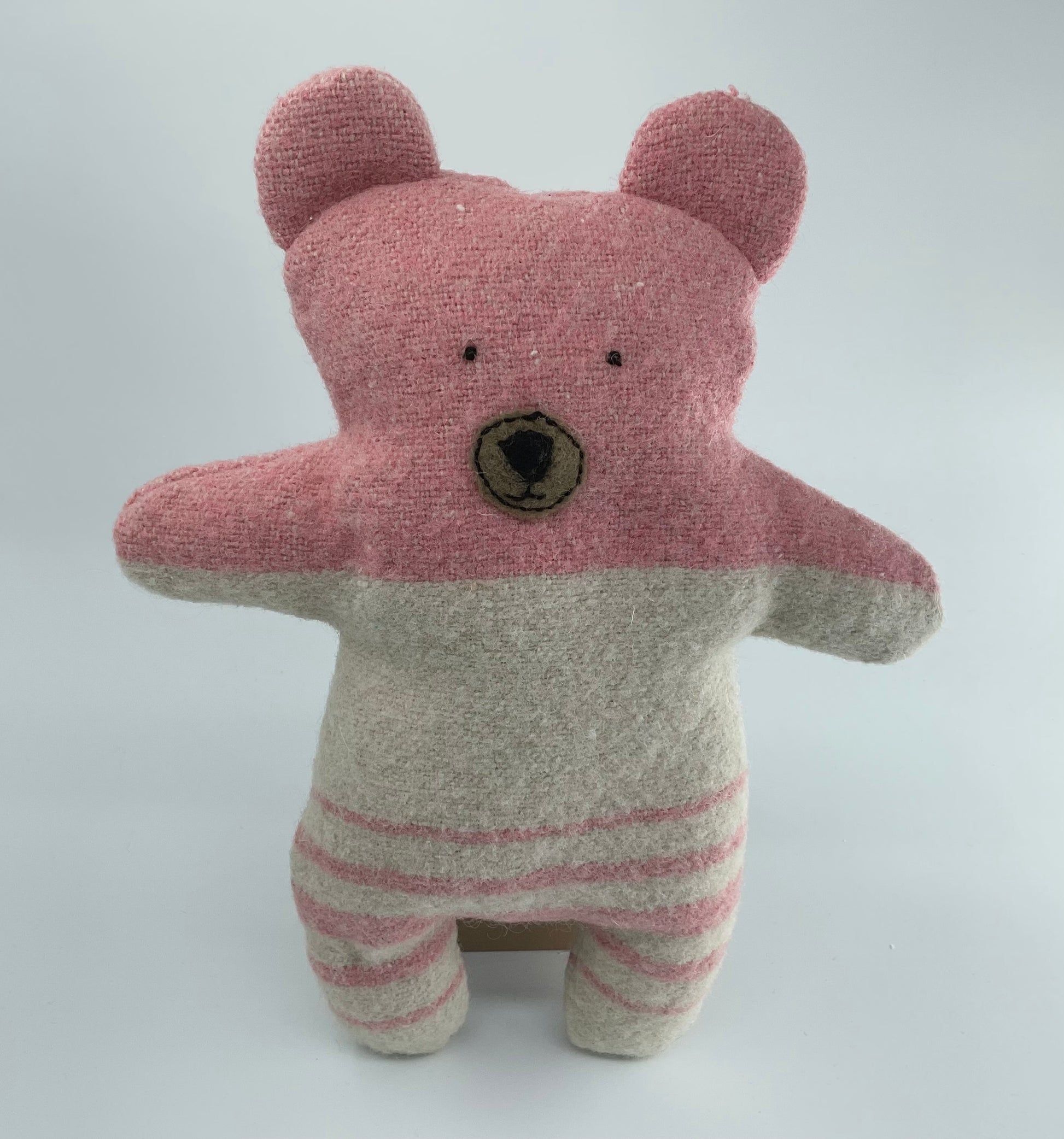 Stuffed teddy bear with pink top and striped legs on a white background