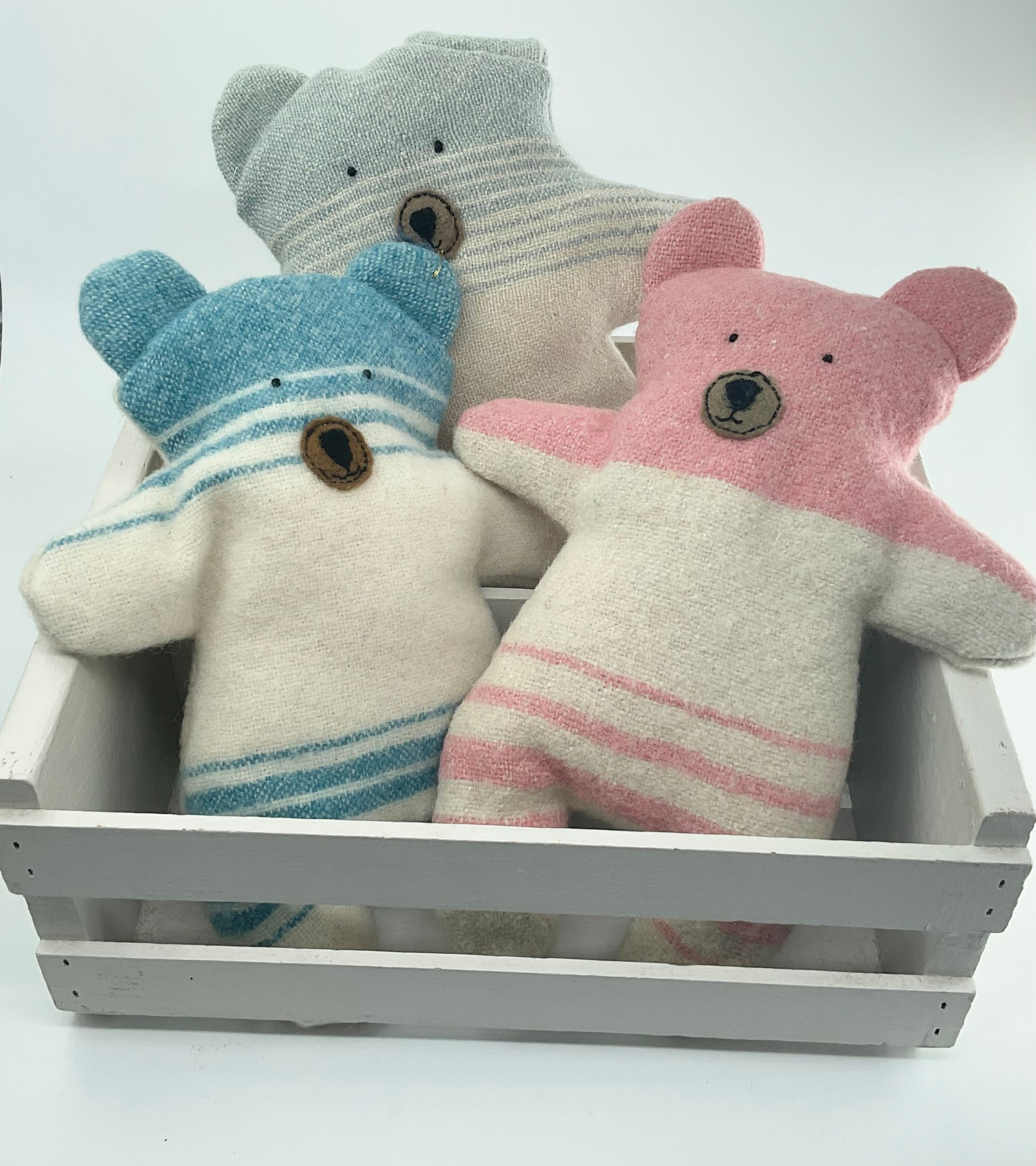Three teddy bears with striped patterns in a white crate on a light gray background