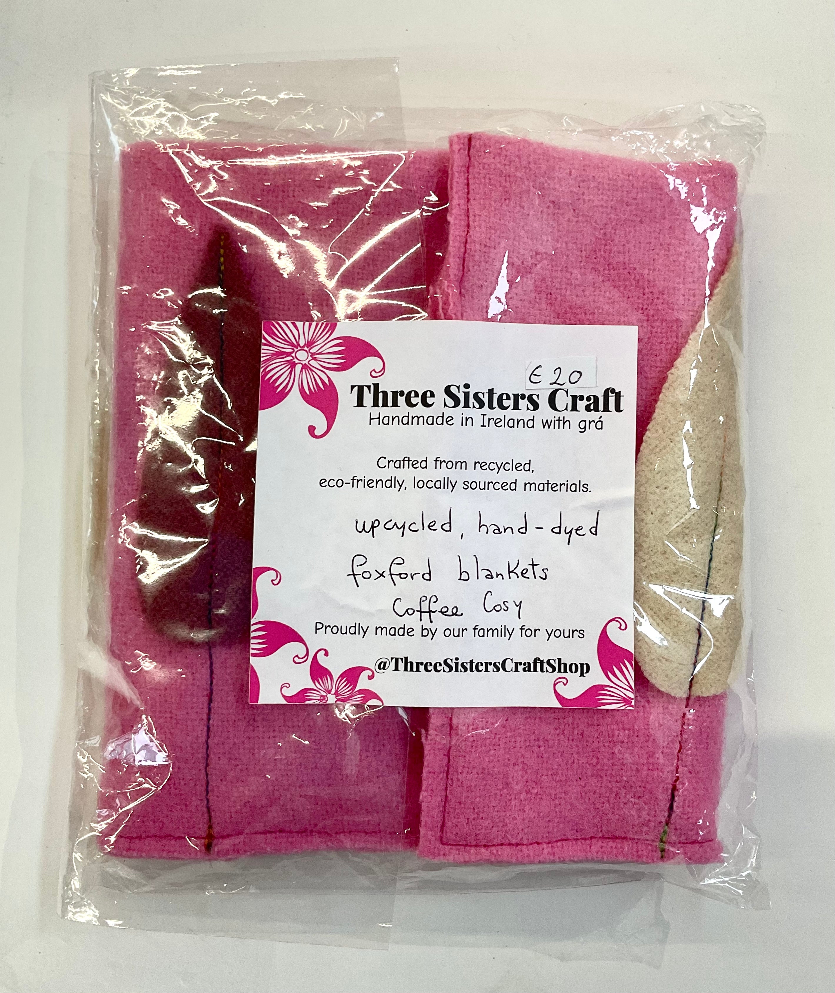 Pink coffee cosie with a 'Three Sisters Craft' label on a white background