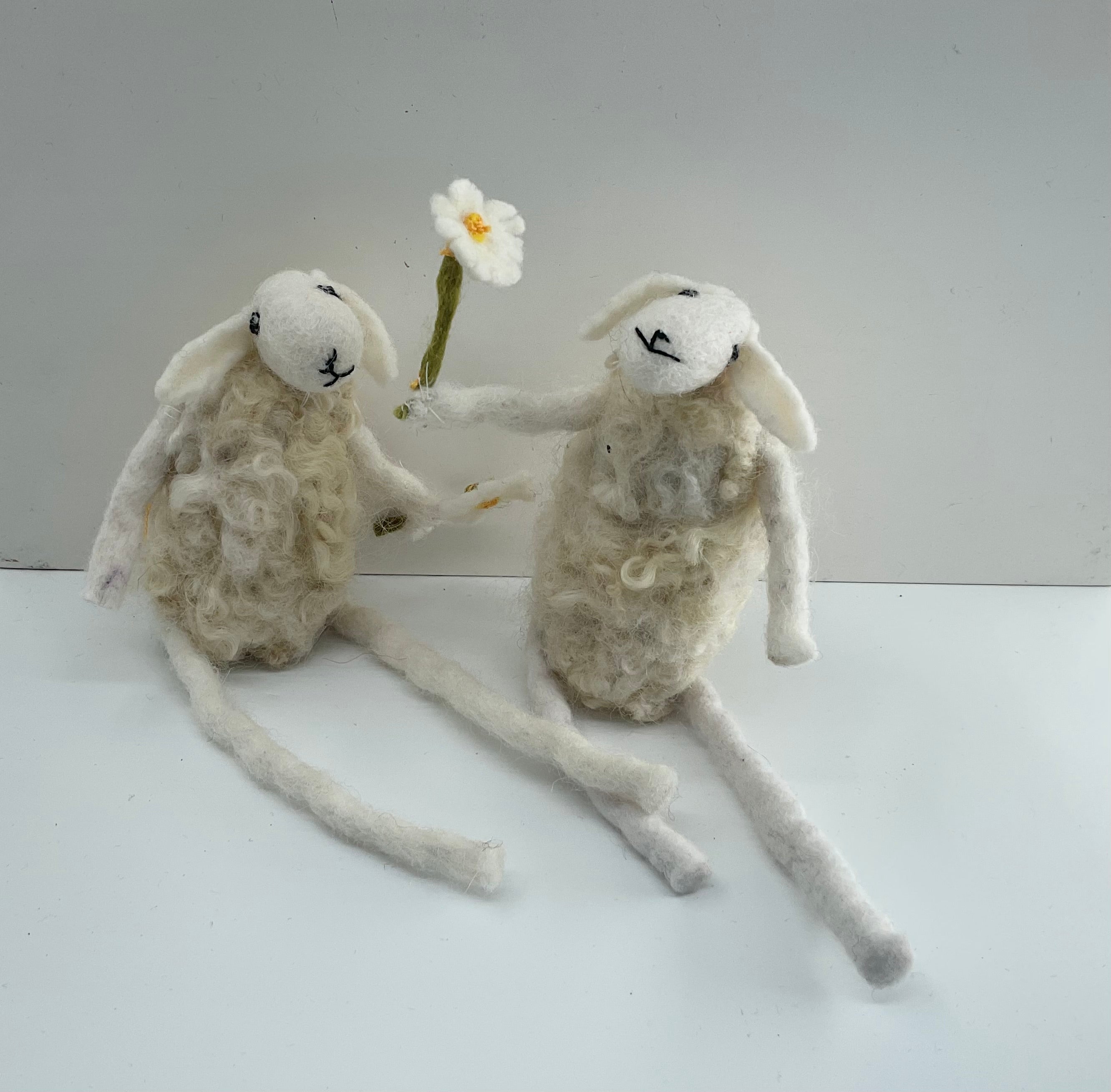 Two handmade felted sheep with one holding a flower on a white background