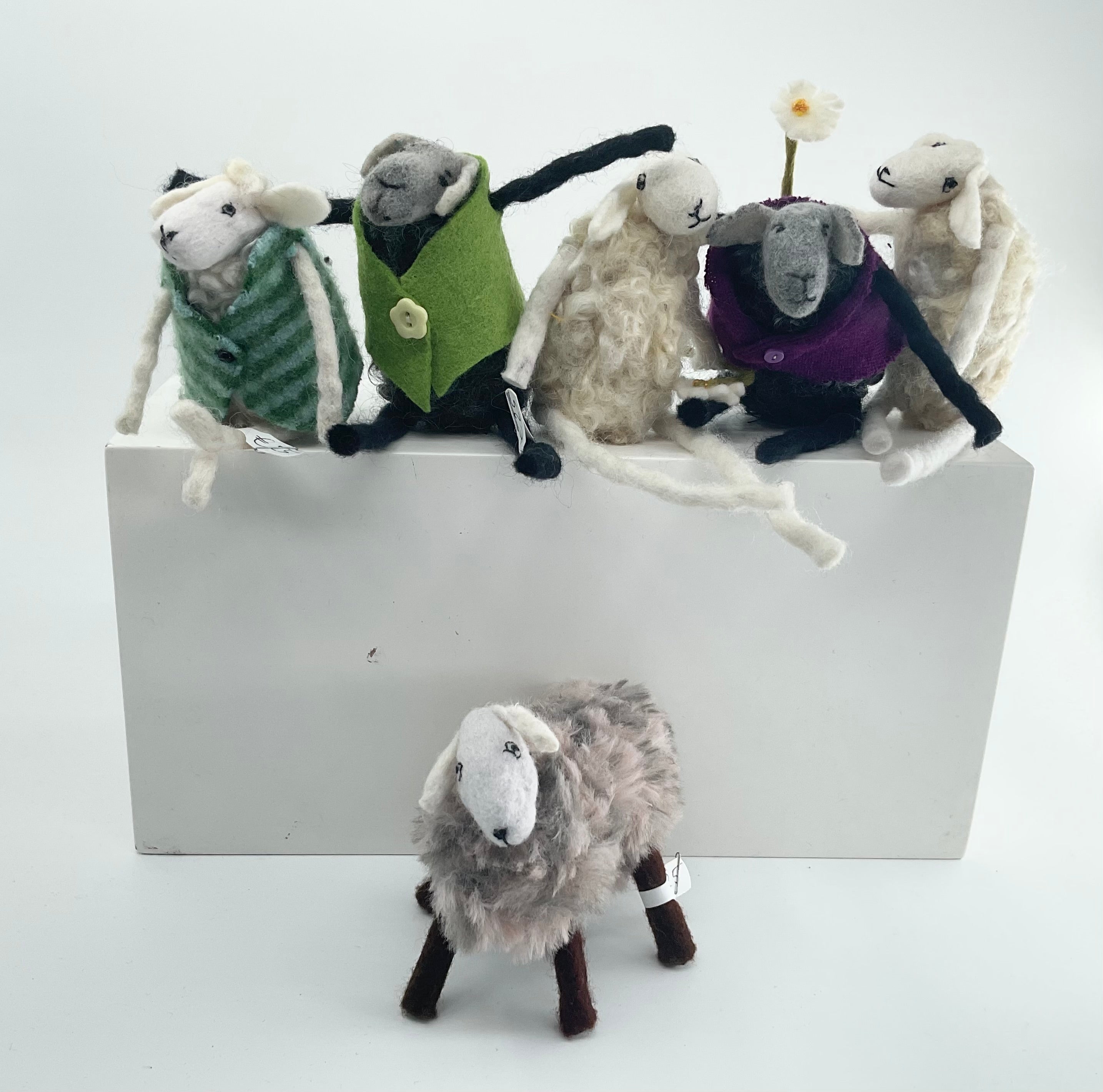 Collection of felted sheep with various accessories on a white block