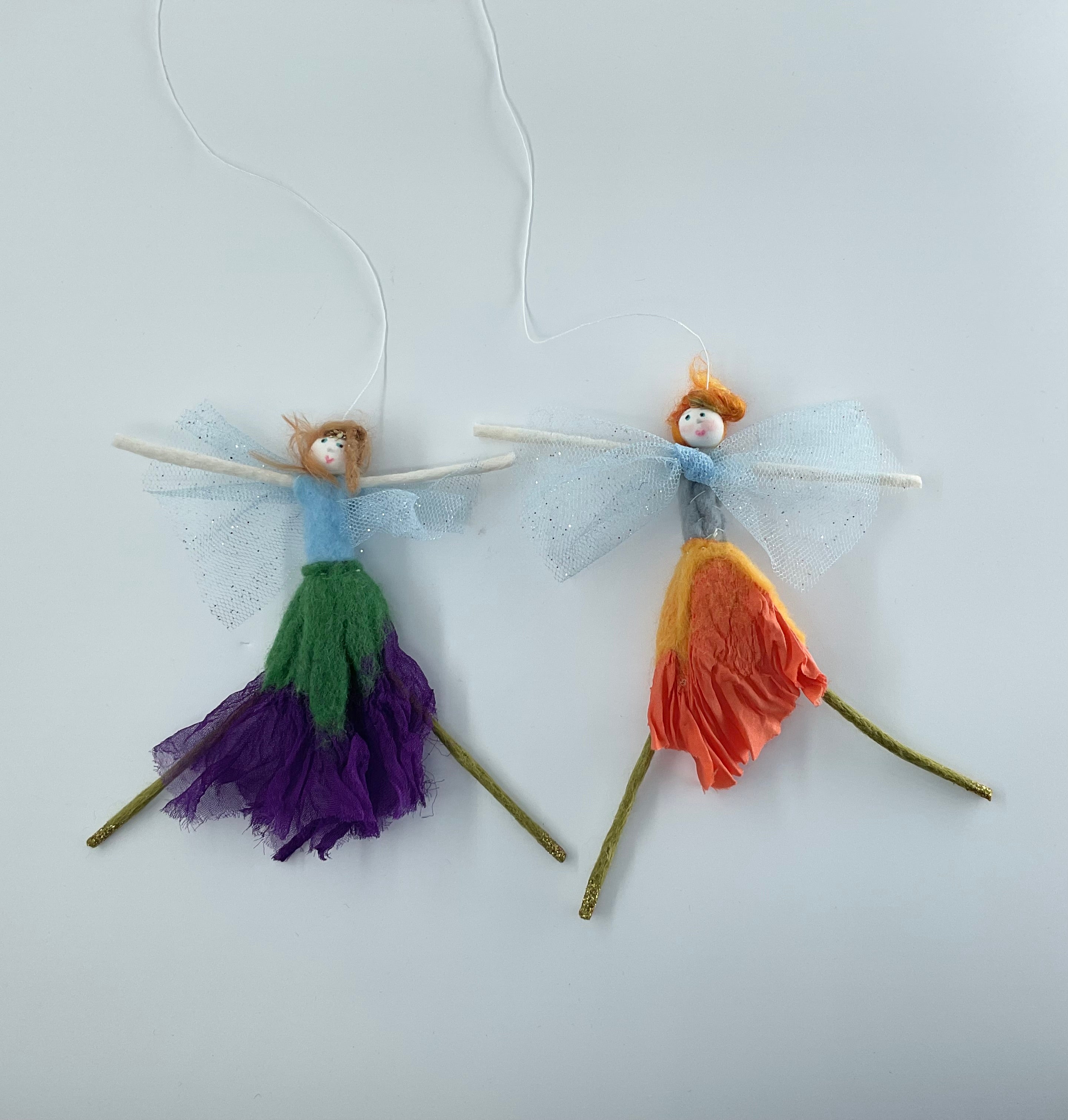 Two colorful fairy figurines on sticks against a light background